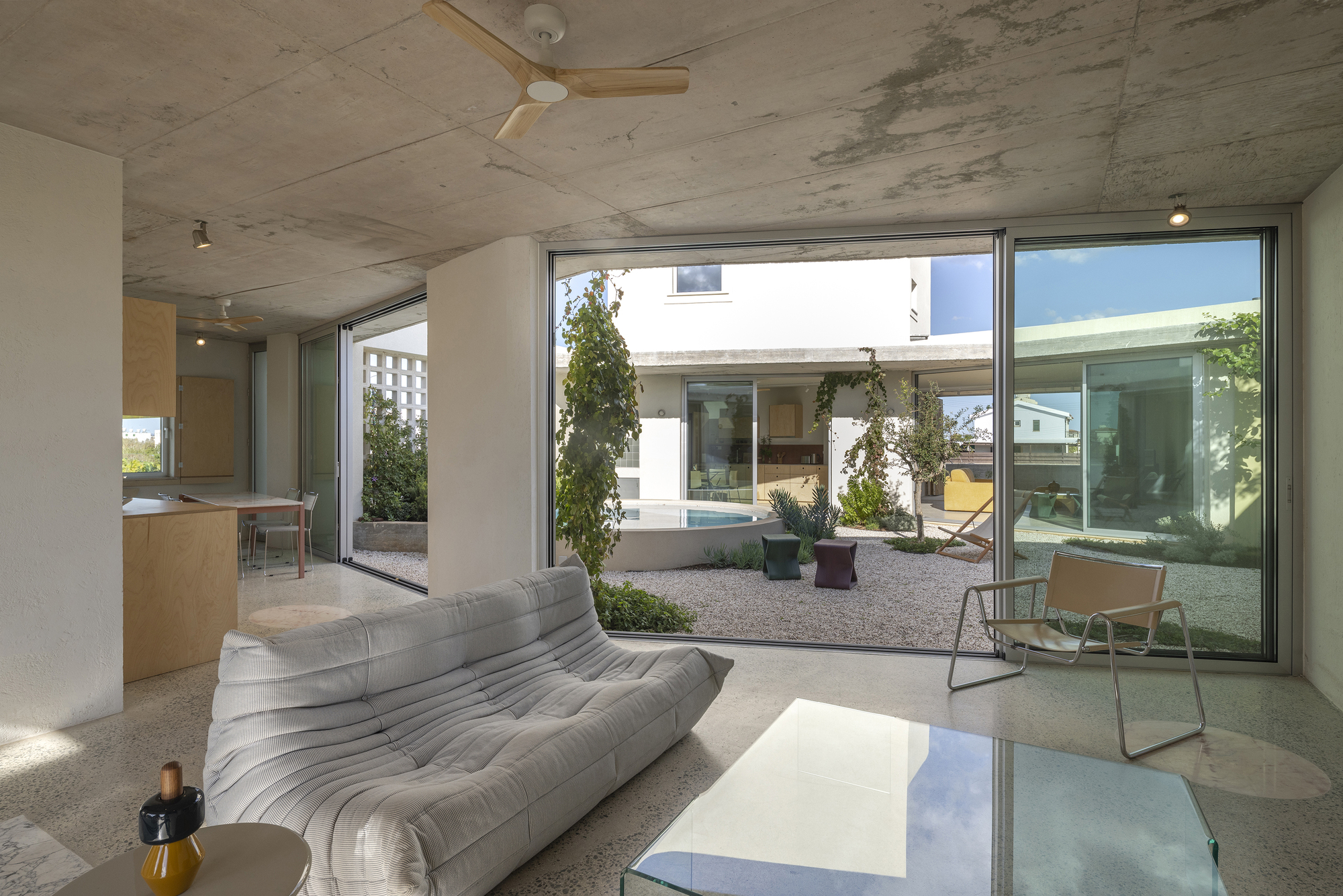 Living room with a grey modular sofa and glass coffee table facing the courtyard through floor-to-ceiling sliding doors