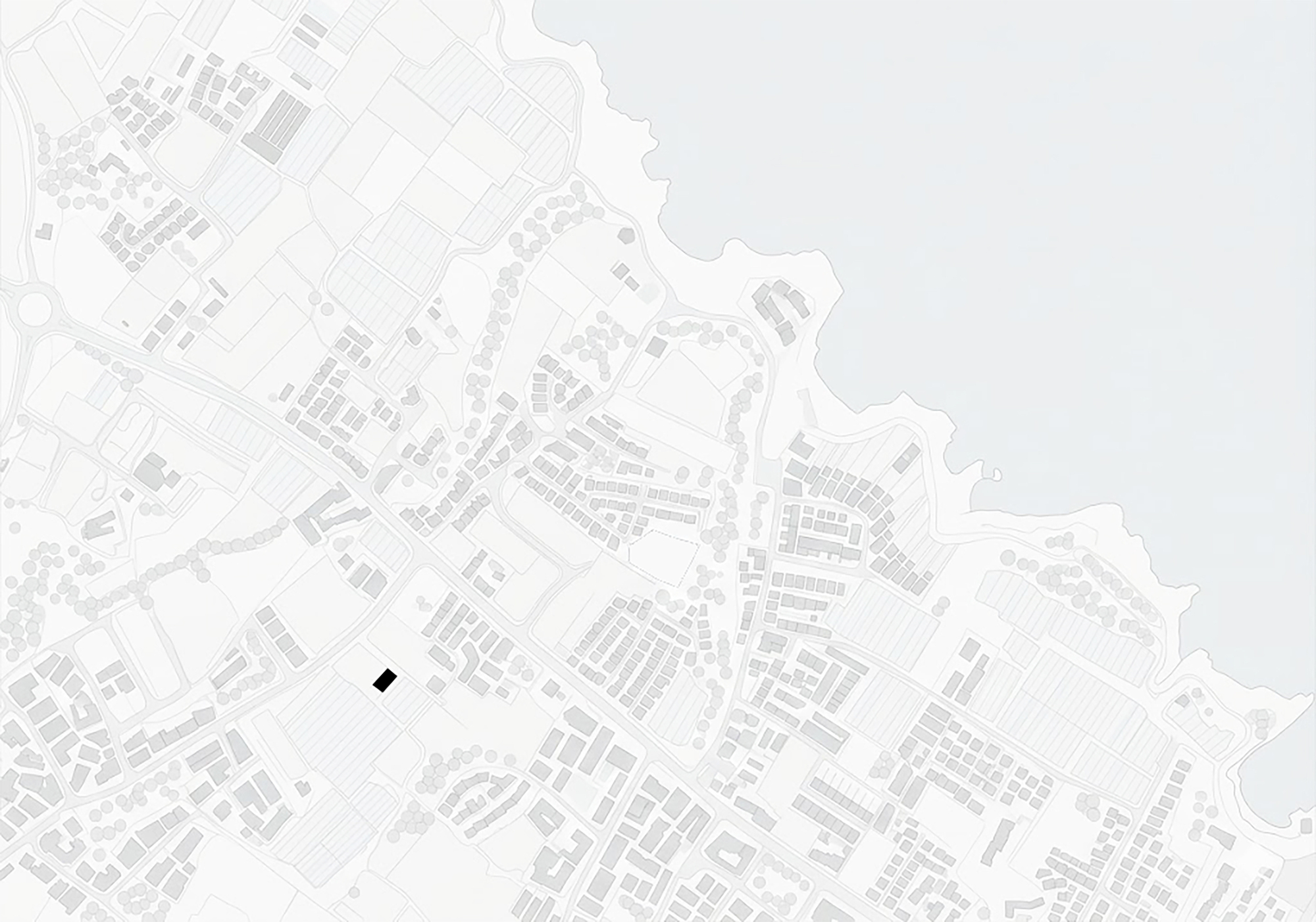 Site plan drawing showing a single black building footprint among surrounding streets, fields and houses beside a coastline