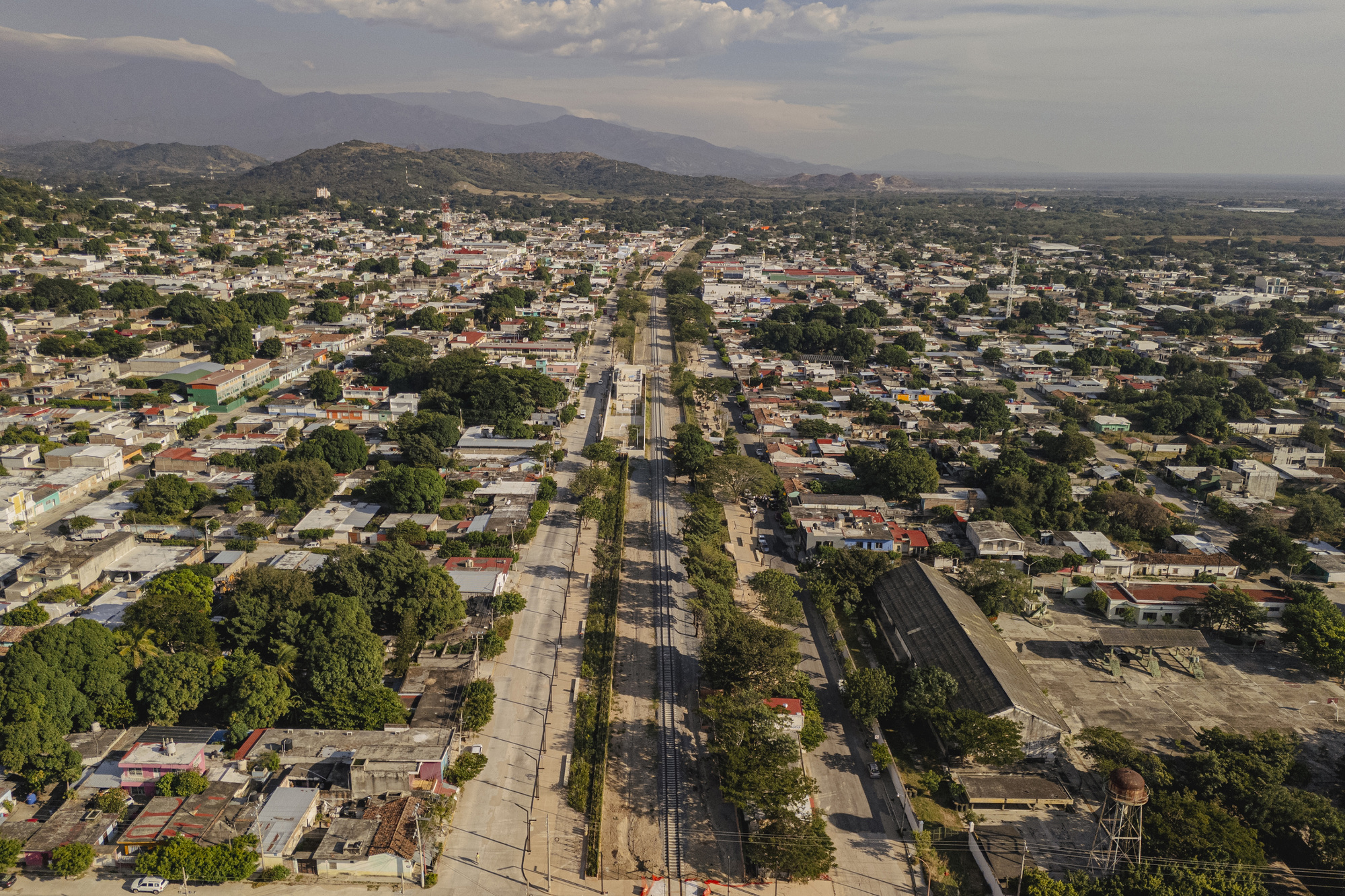 Aerial view of a railway line running straight through a low-rise town with tree-lined streets and mountains on the horizon