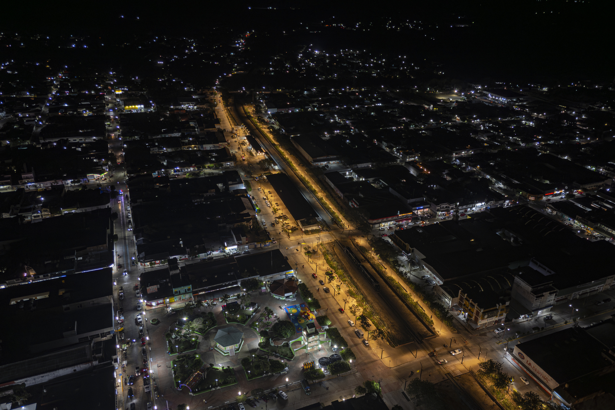 Night aerial view of a town grid with a lit linear park running down the center along the rail corridor