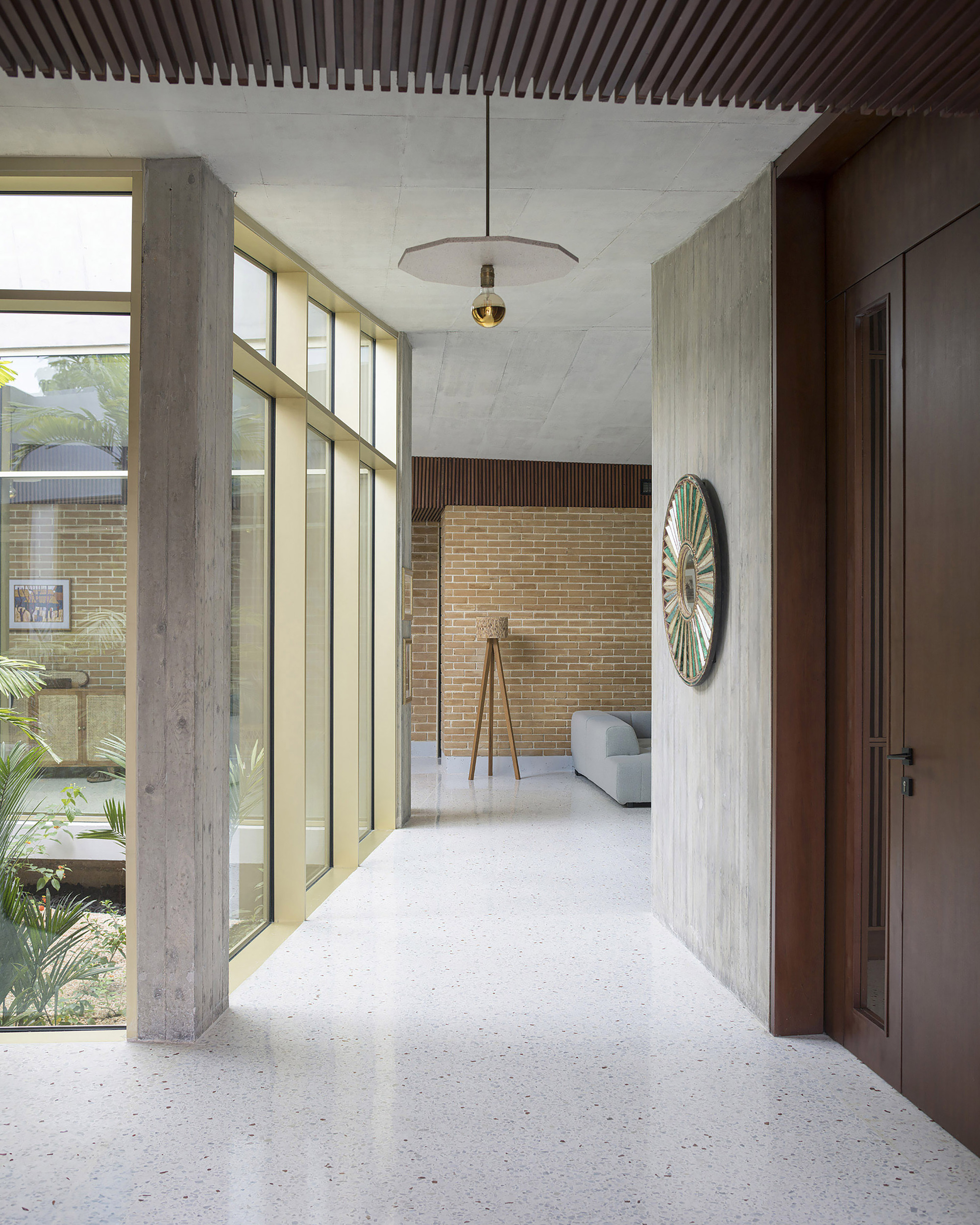 Entry corridor with board-marked concrete wall, timber door and round wall ornament, light falling through a tall glazed screen
