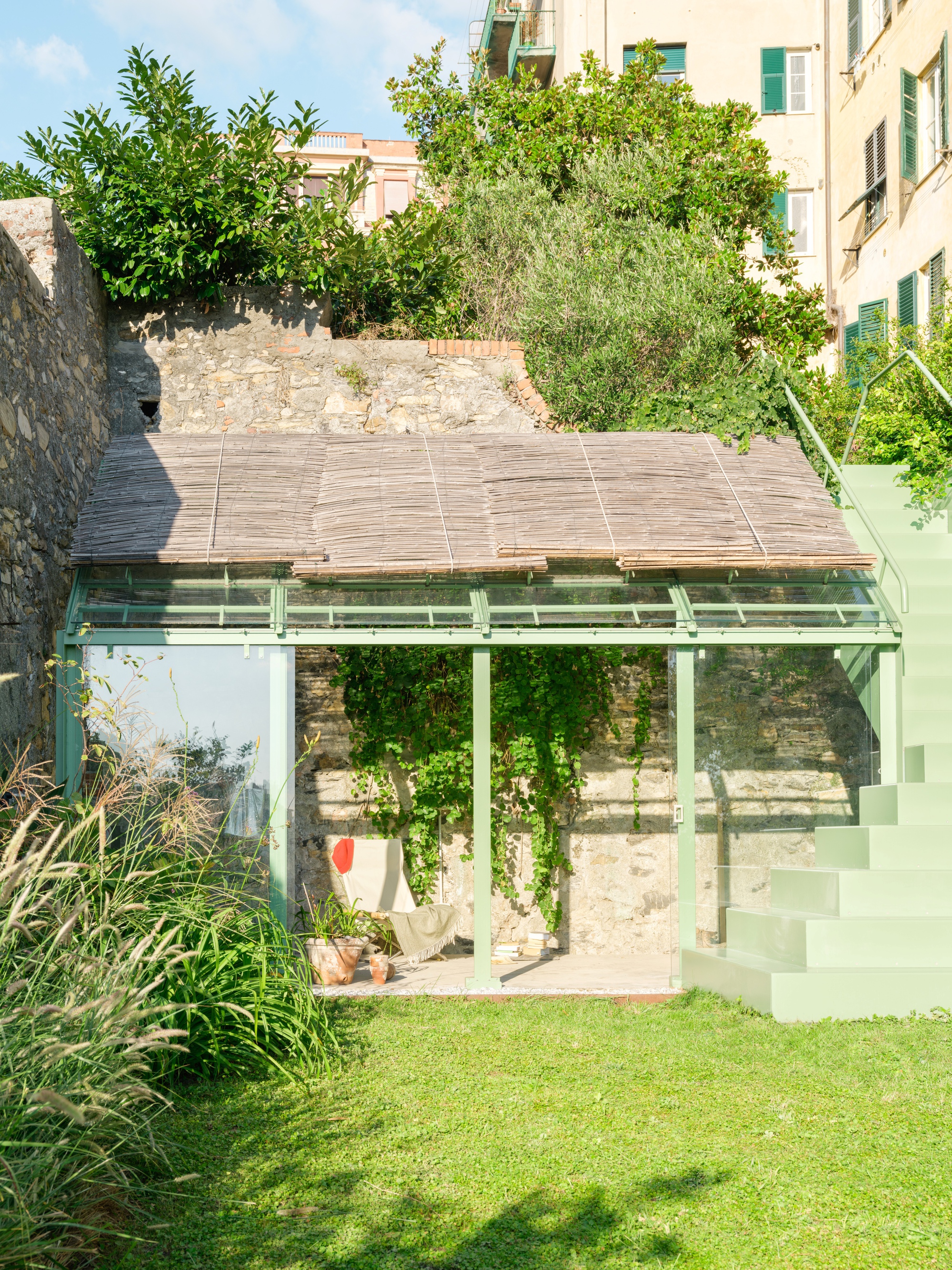 Front of the glazed pavilion with its thatched reed roof and green steel frame, with a staircase climbing the right side