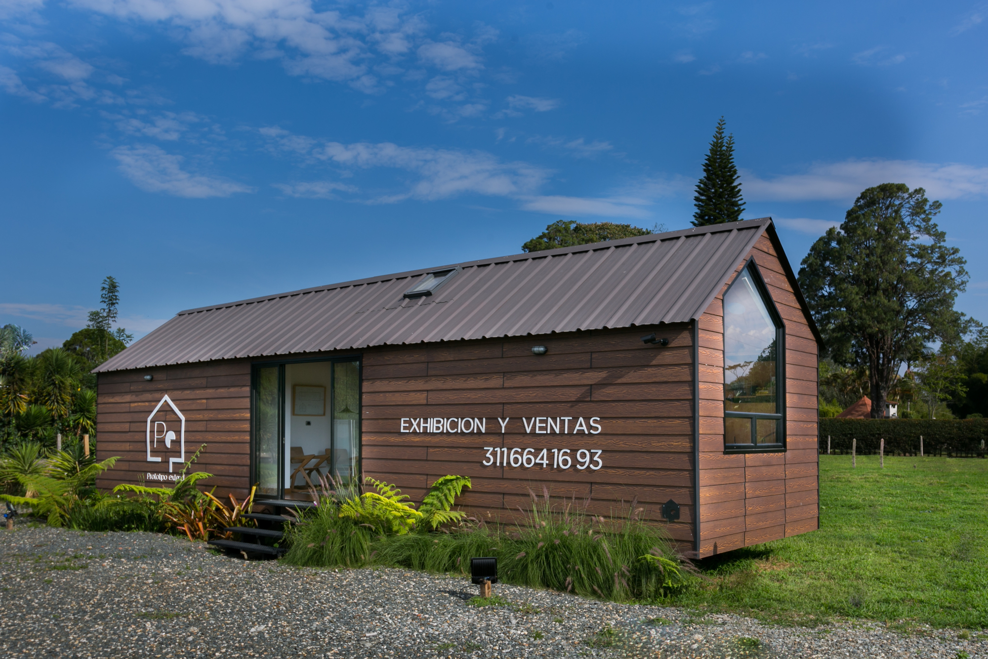 Three-quarter view of the timber-clad cabin with its gabled end window, metal roof and gravel foreground under a deep blue sky