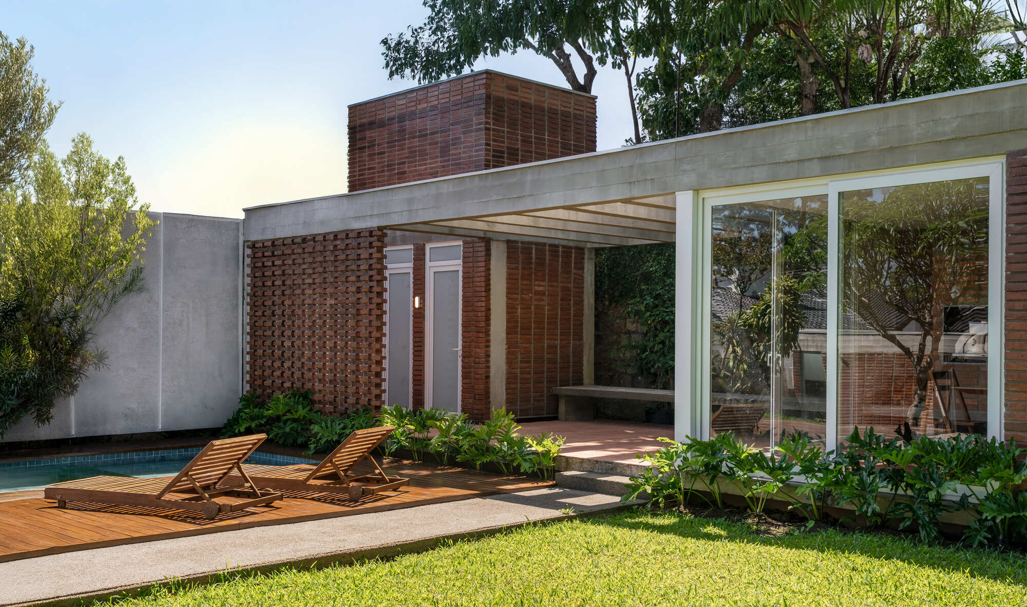 Perforated brick screen wall and concrete roof edge beside a pool deck with two wooden loungers in late afternoon light