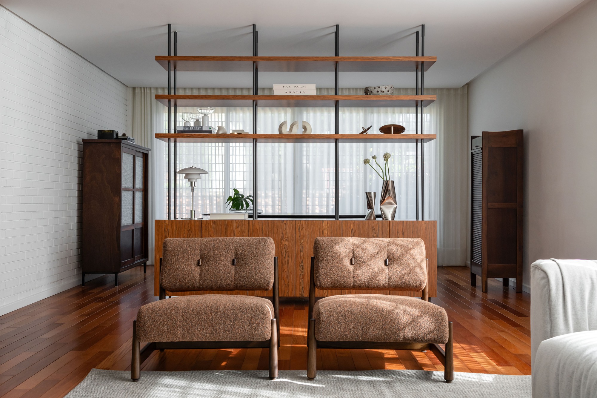 Two bouclé lounge chairs facing the shelving divider, with afternoon sun falling across the wood floor