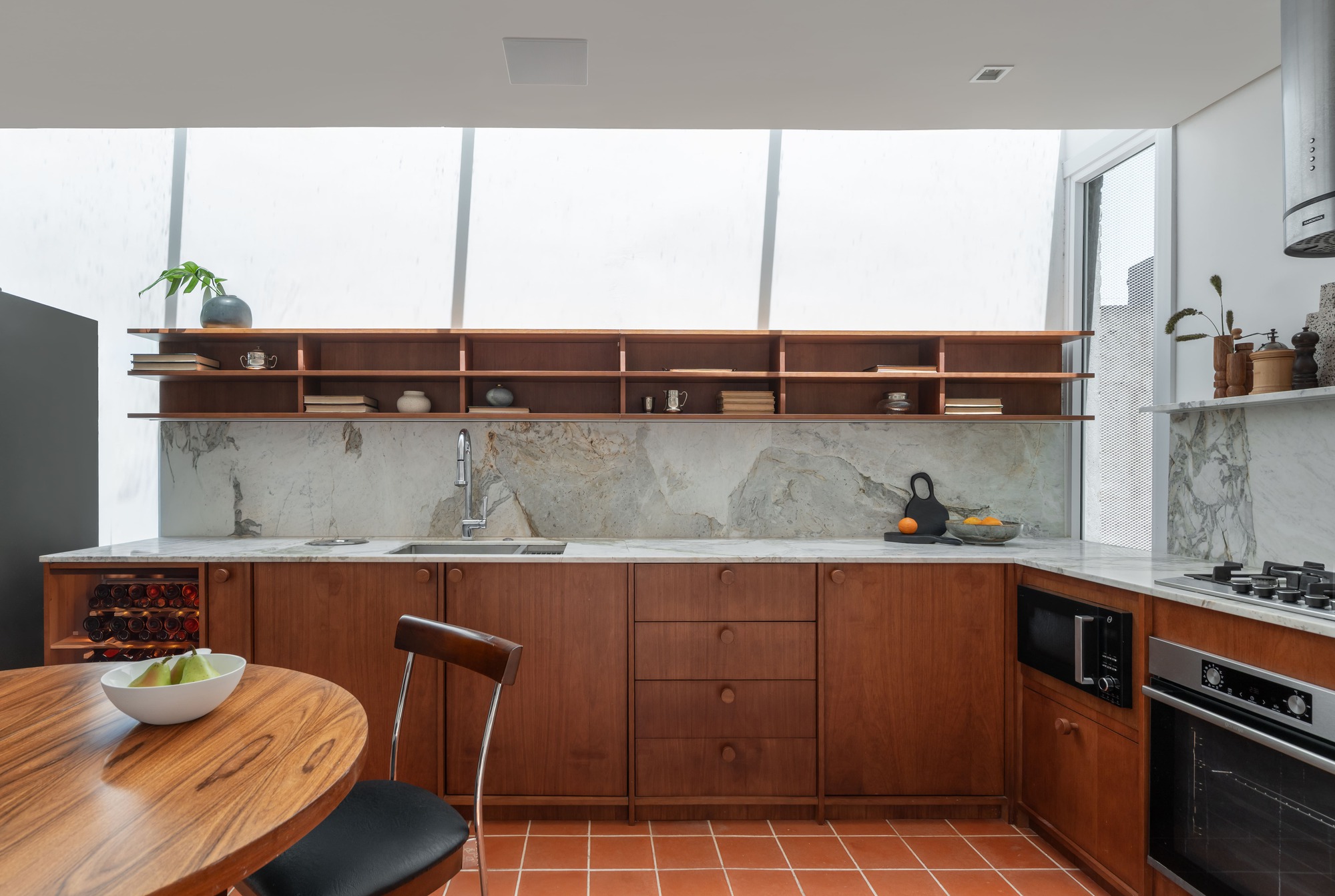 Kitchen with walnut cabinets, marble backsplash and open shelves under a slanted skylight, terracotta tile floor below