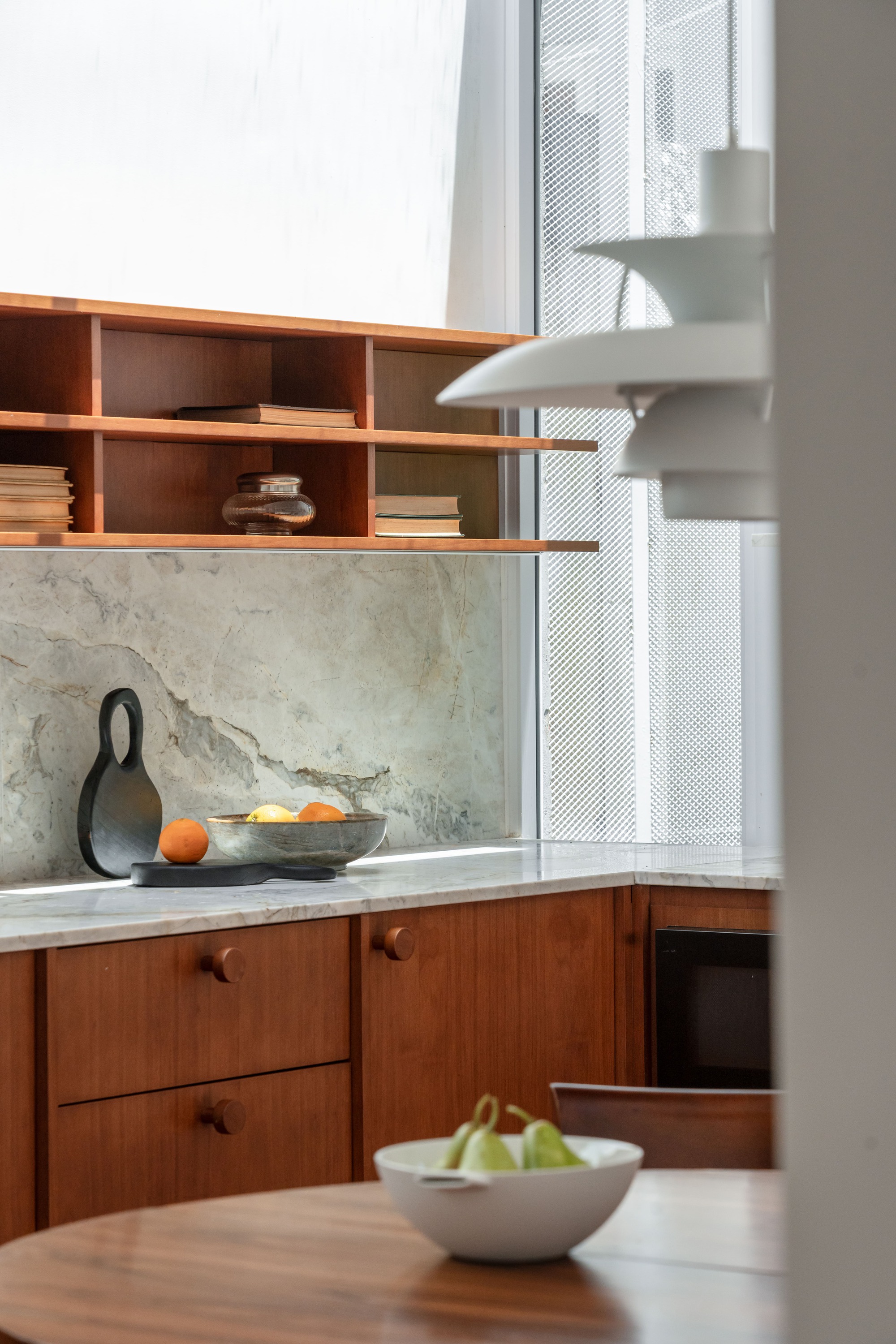 Close view of kitchen shelves and marble backsplash with a bowl of pears on the round table in the foreground