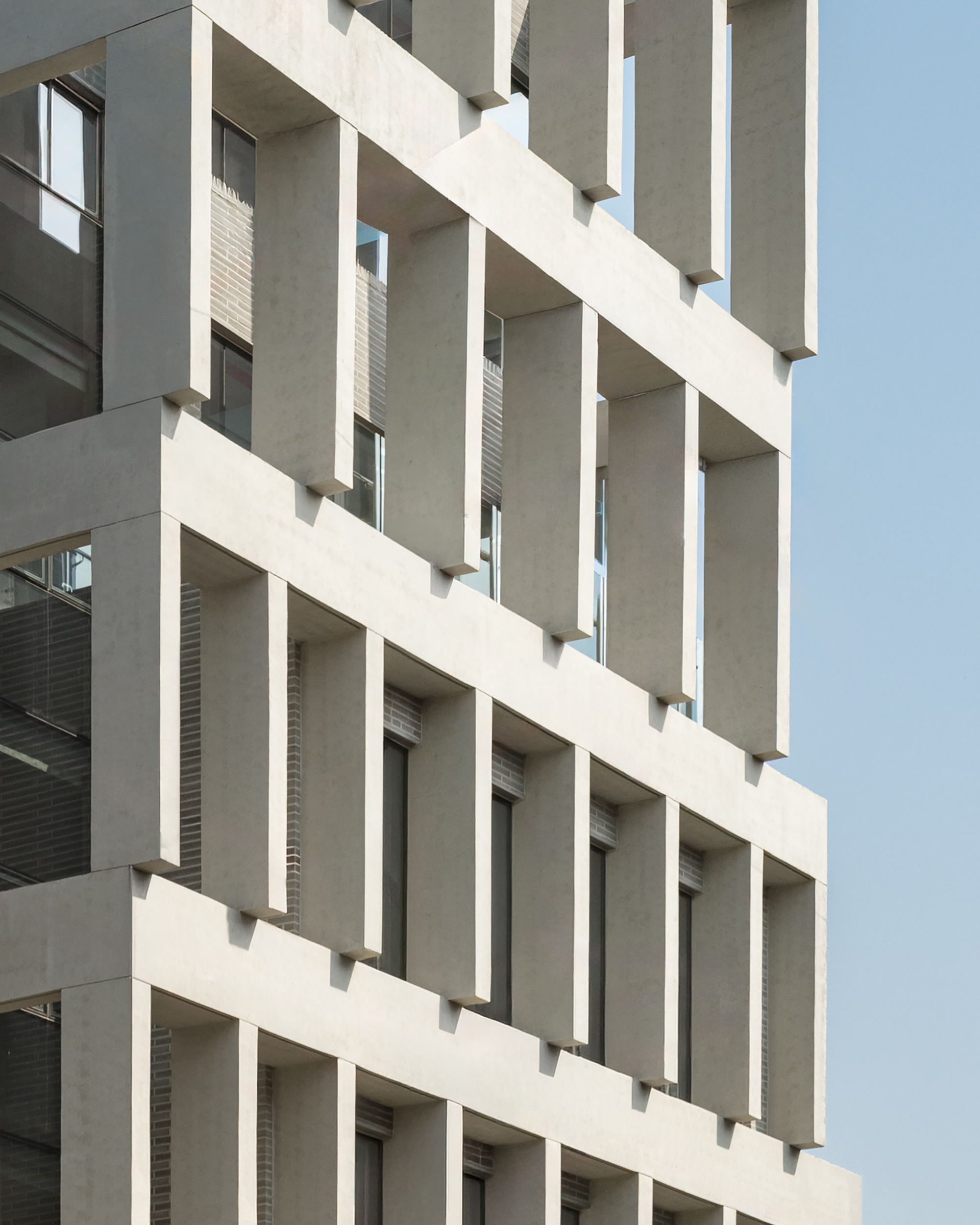 Close-up of staggered concrete fins casting sharp shadows on the facade against a pale blue sky
