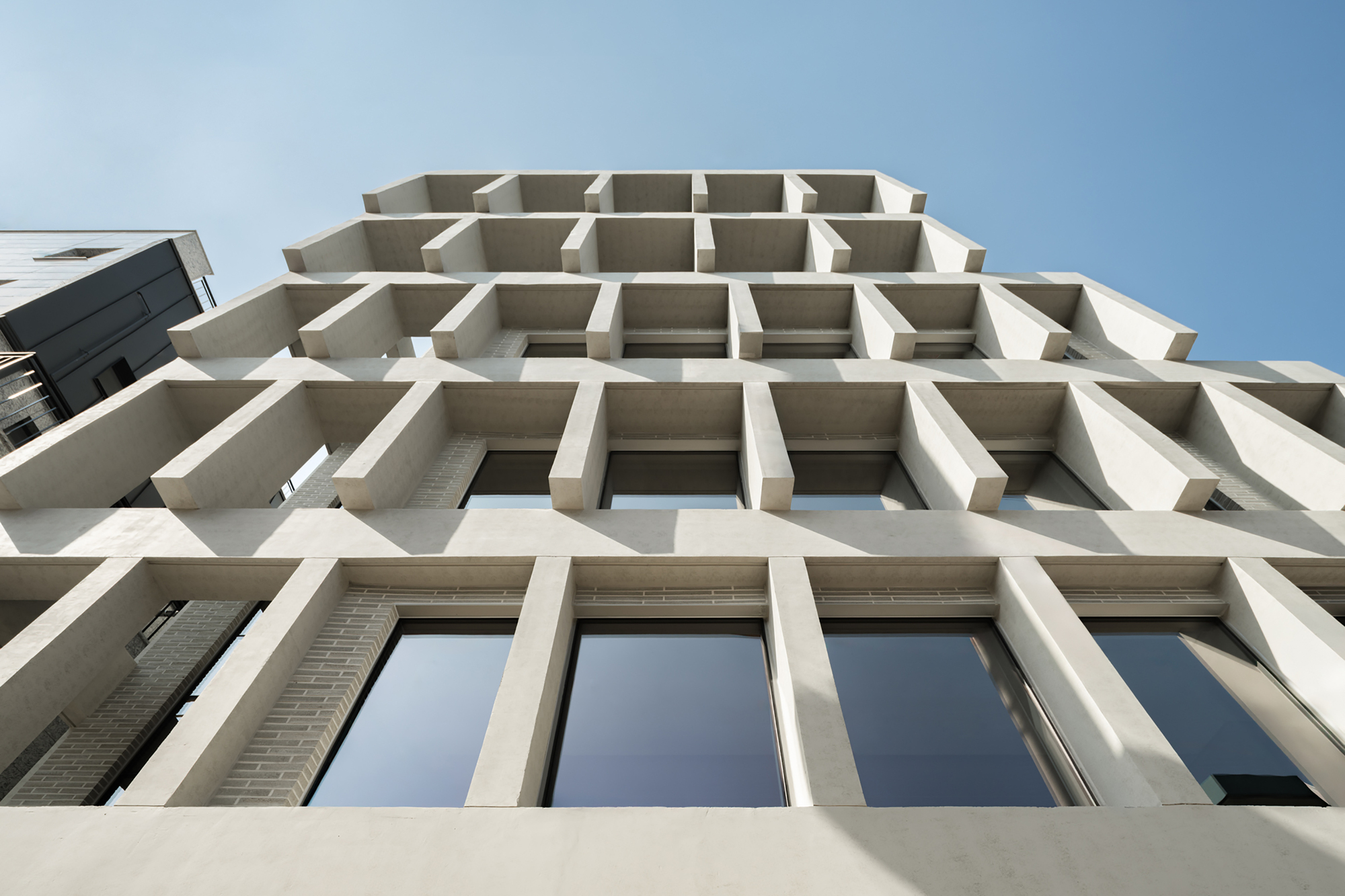 Low angle looking up at the grid of deep concrete fins and glazed bays against a pale blue sky