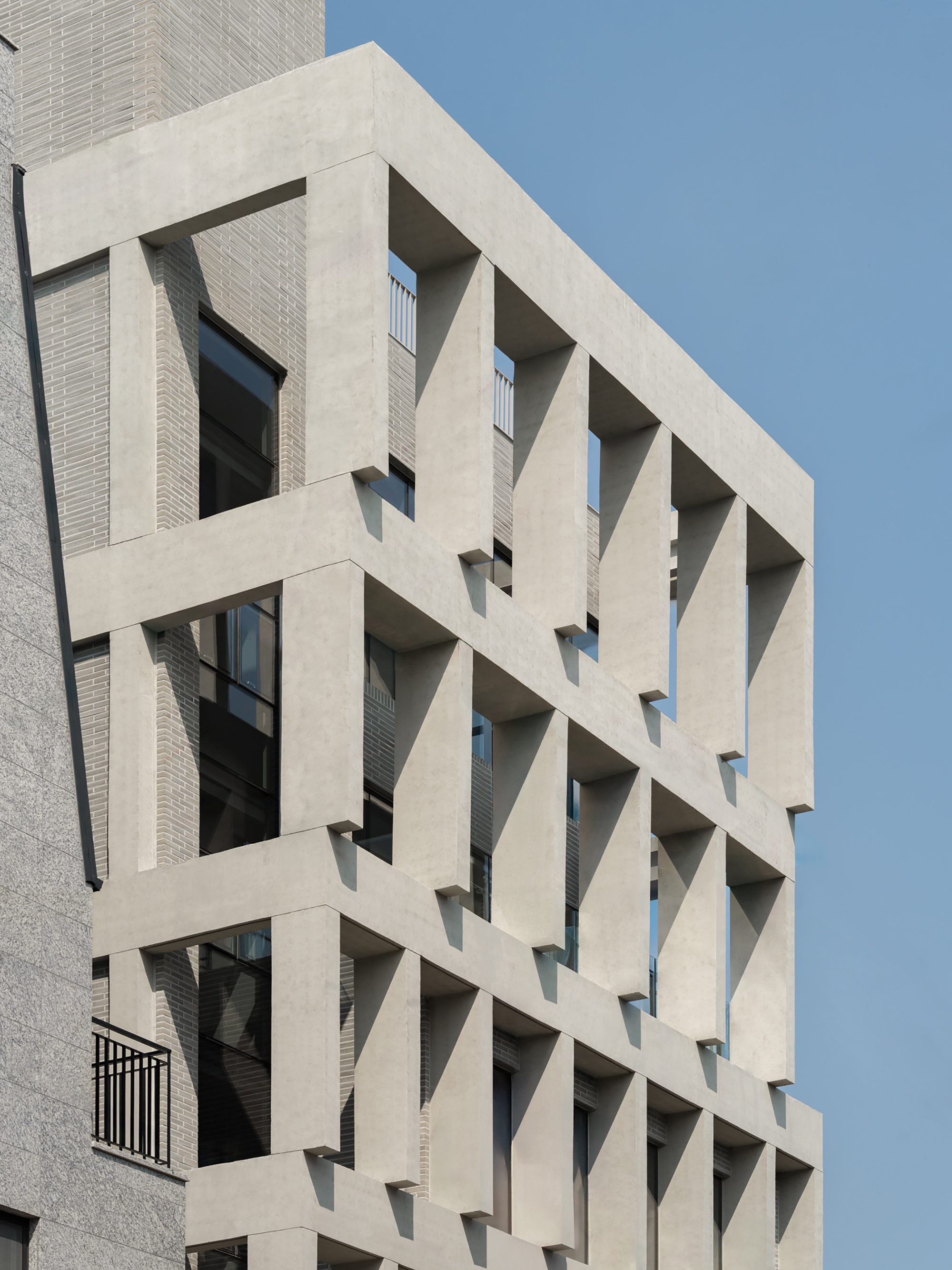 Side view of the top floors where angled concrete fins cast sharp shadows over the brick infill in afternoon sun