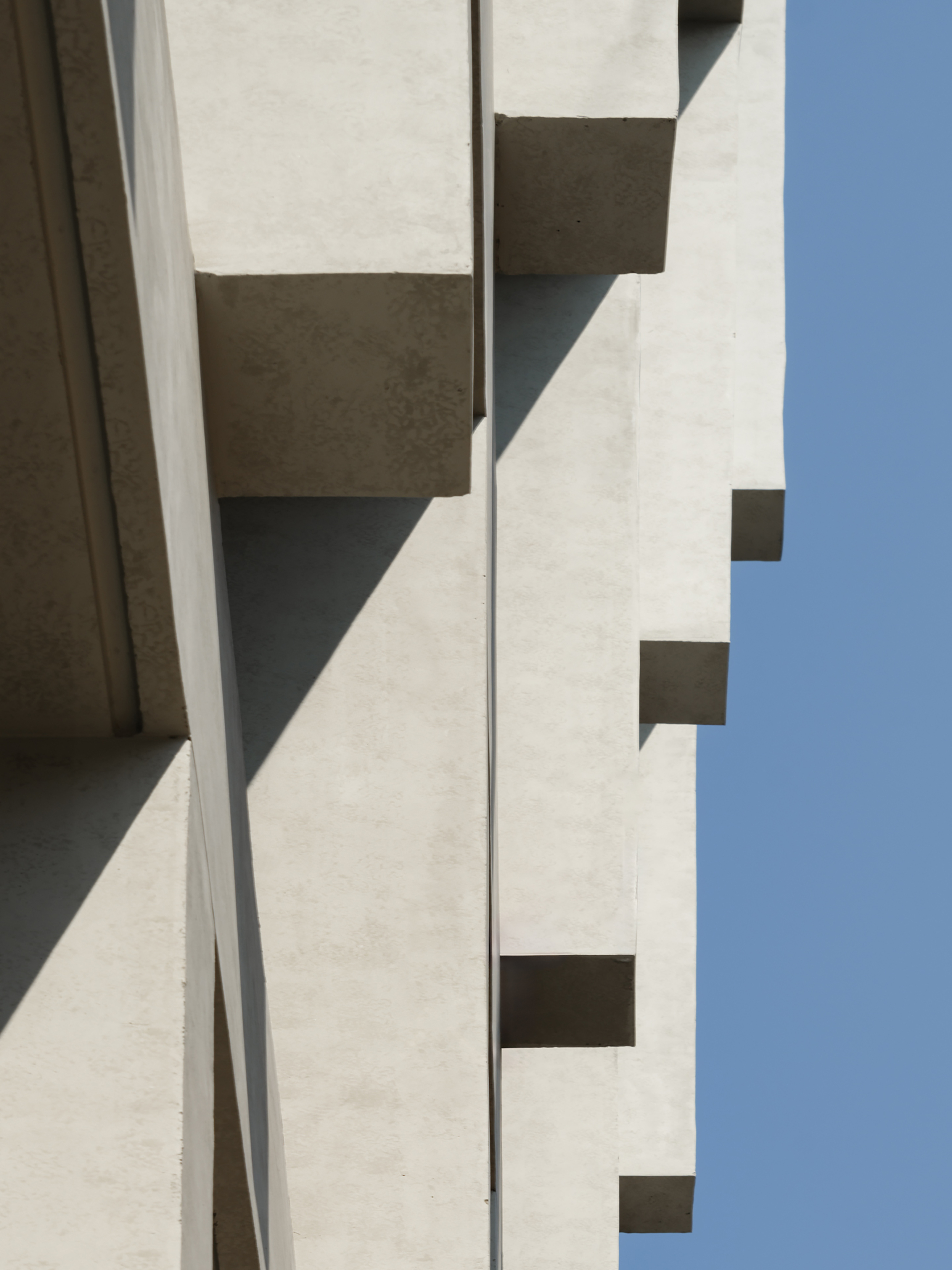 Close-up of stacked concrete fin ends with hard diagonal shadows against a deep blue sky
