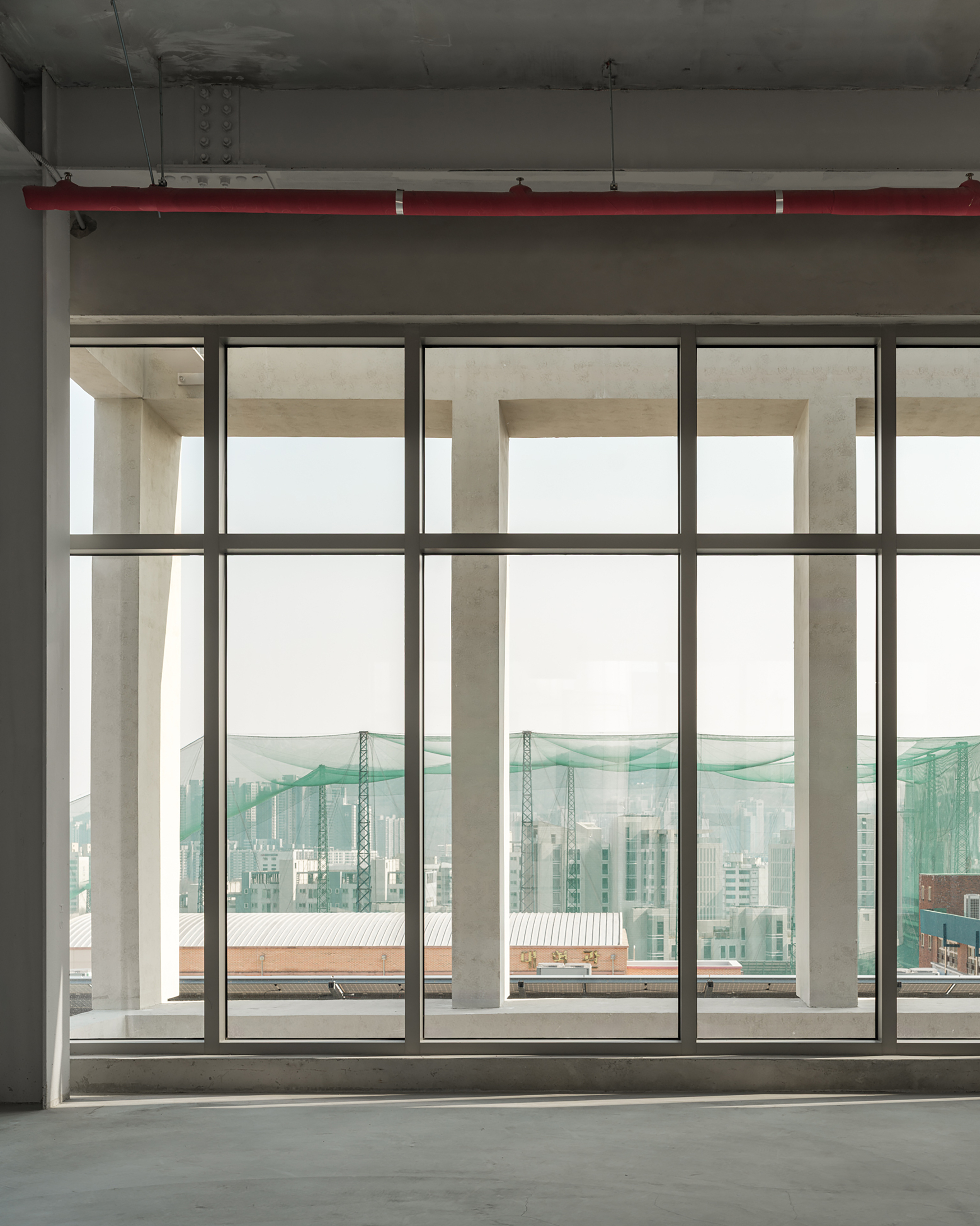Gridded window wall framing concrete outrigger columns and a green netting structure beyond, in soft afternoon haze