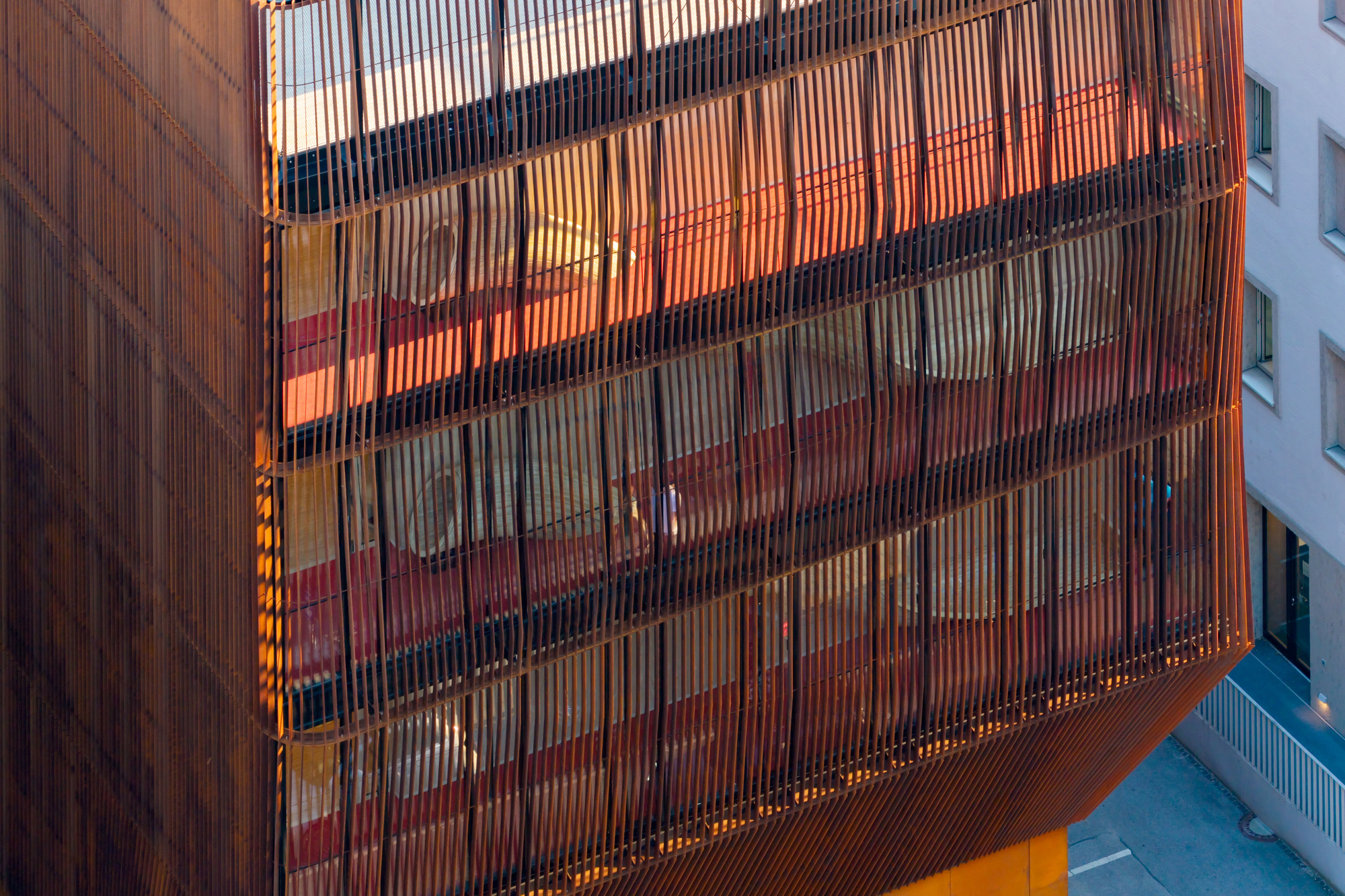 Close-up of the copper-toned vertical slat facade at dusk, with red interior surfaces glowing behind the screen