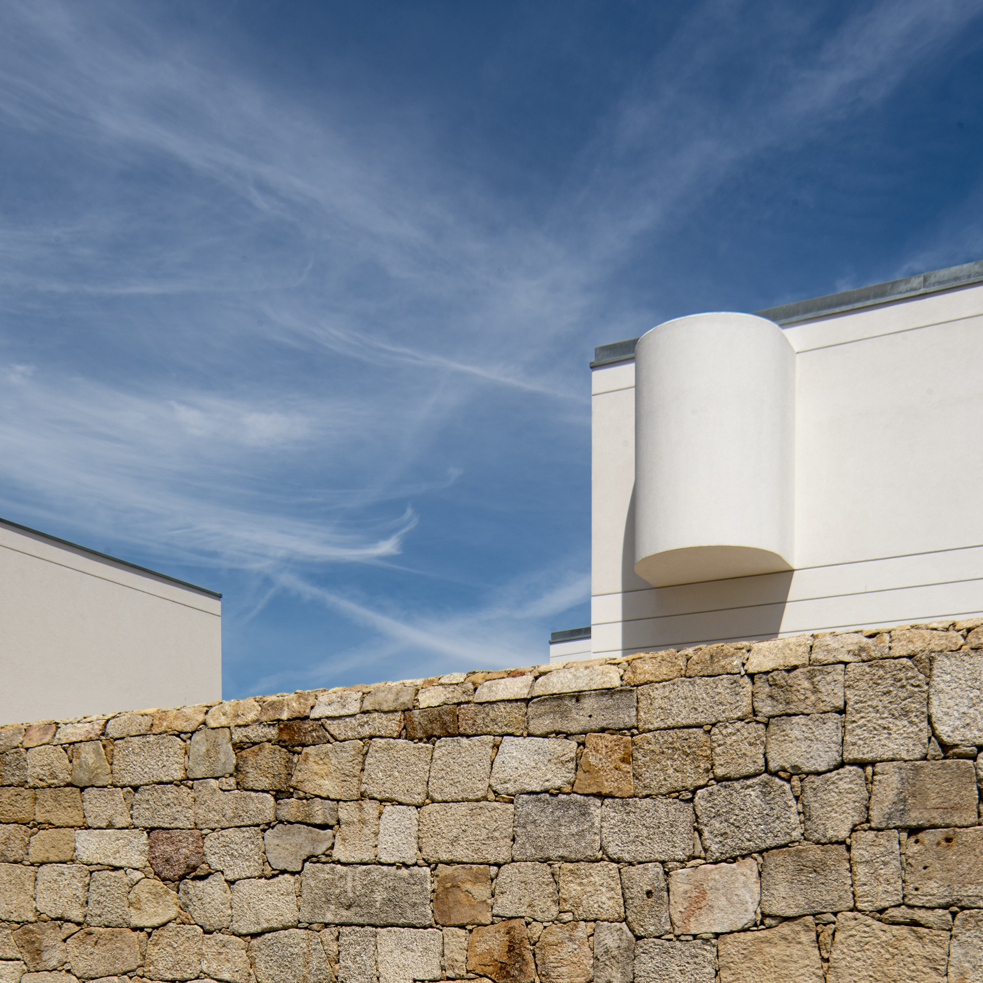 Rounded white drum bay rising above a rough granite wall, with thin cirrus streaks across the sky