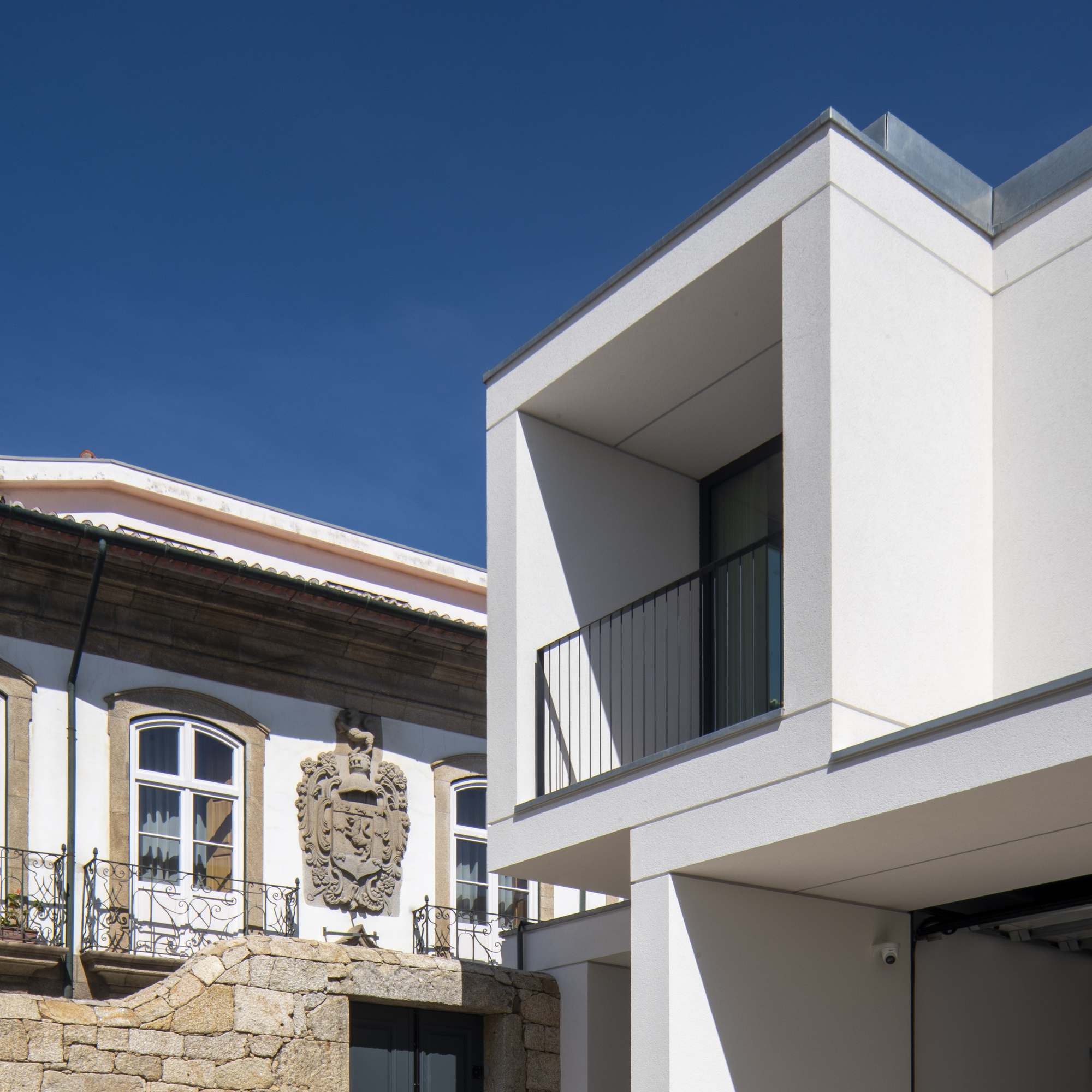 Corner of the white balcony volume set against an older facade with a carved stone coat of arms and iron balconies