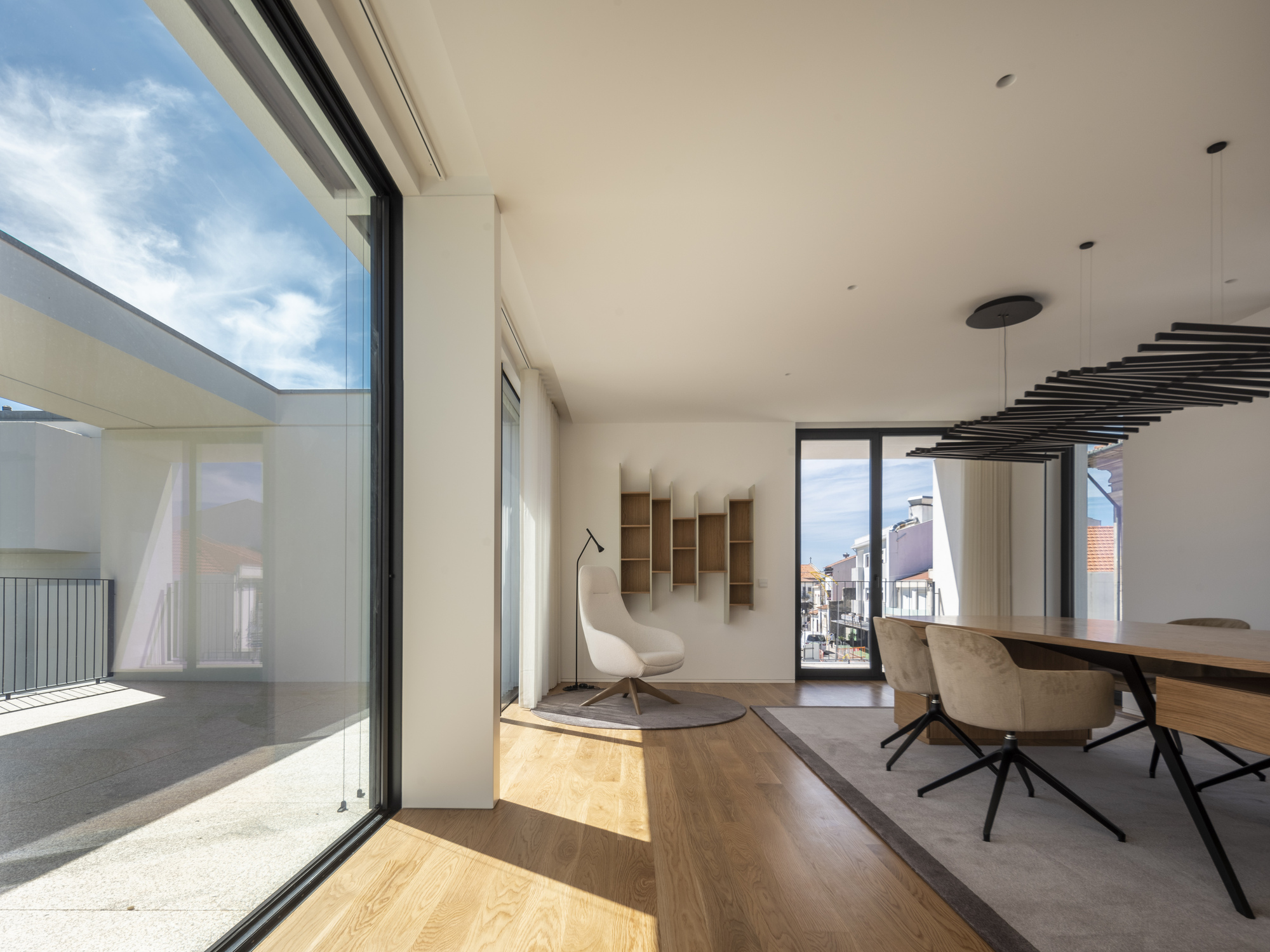 Living and dining area with oak floor, sculptural pendant light and cream armchair beside a sliding glass wall opening to the terrace