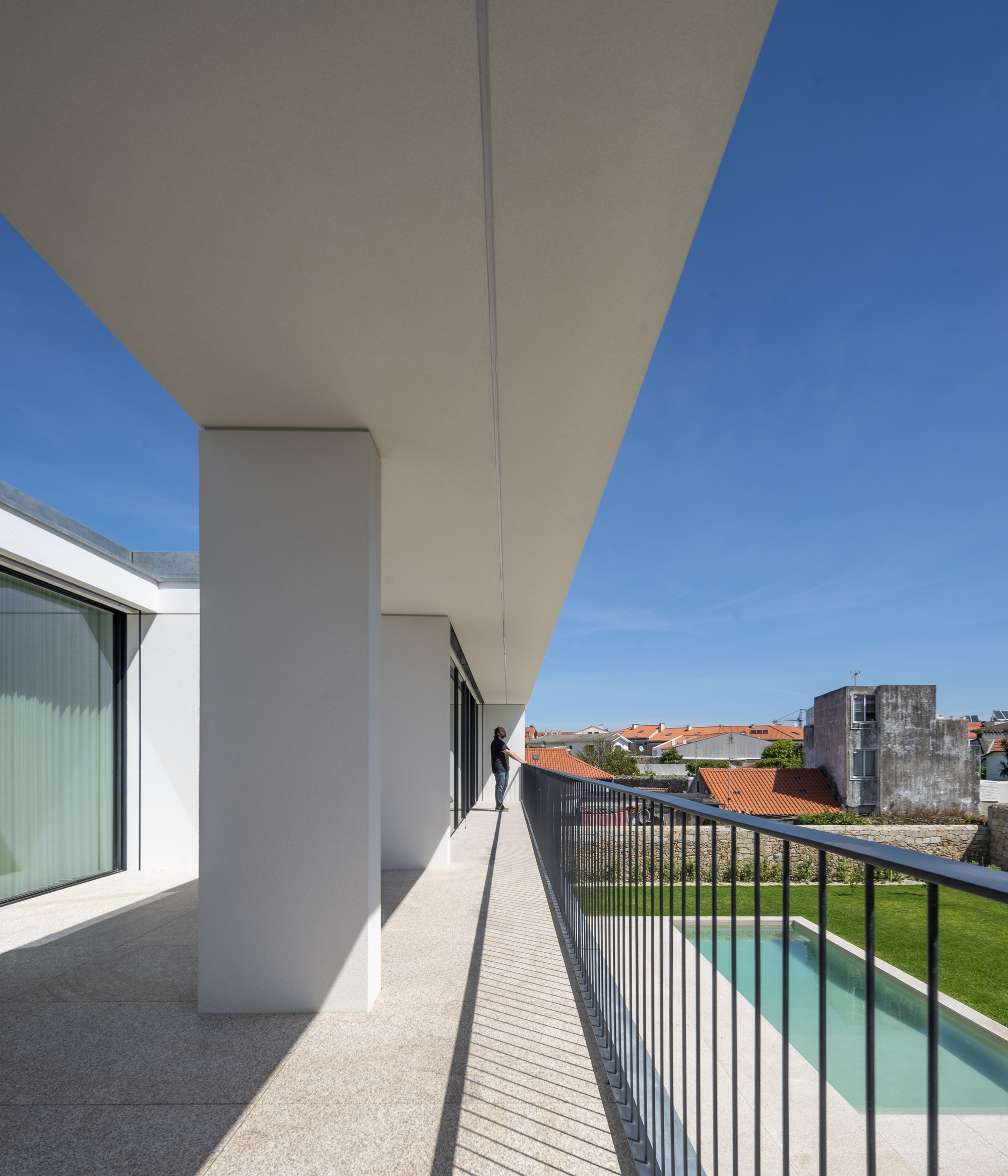 Covered terrace with white columns and granite paving, a person at the metal railing above a lawn and swimming pool