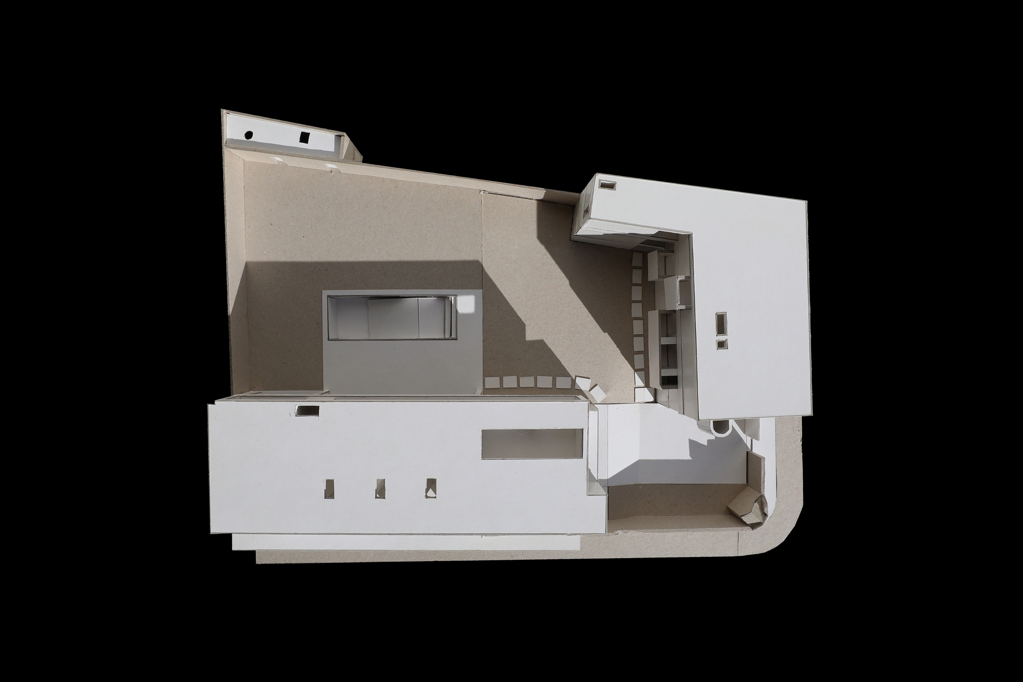 Top-down view of a white cardboard site model showing an L-shaped block, a low wing and a central courtyard against black