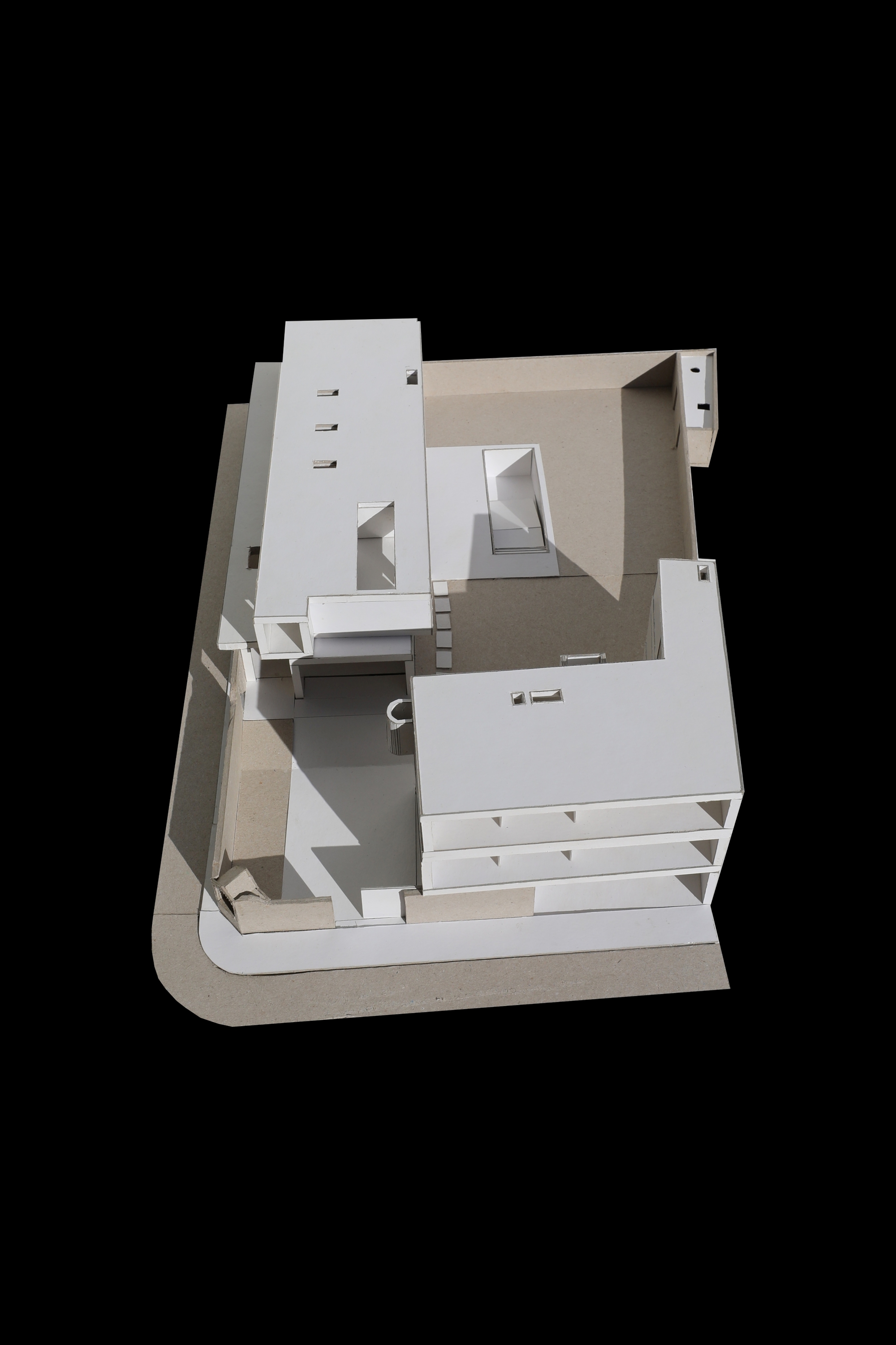 Angled aerial view of a white cardboard massing model with stacked floors, a rounded street corner and an open courtyard on black