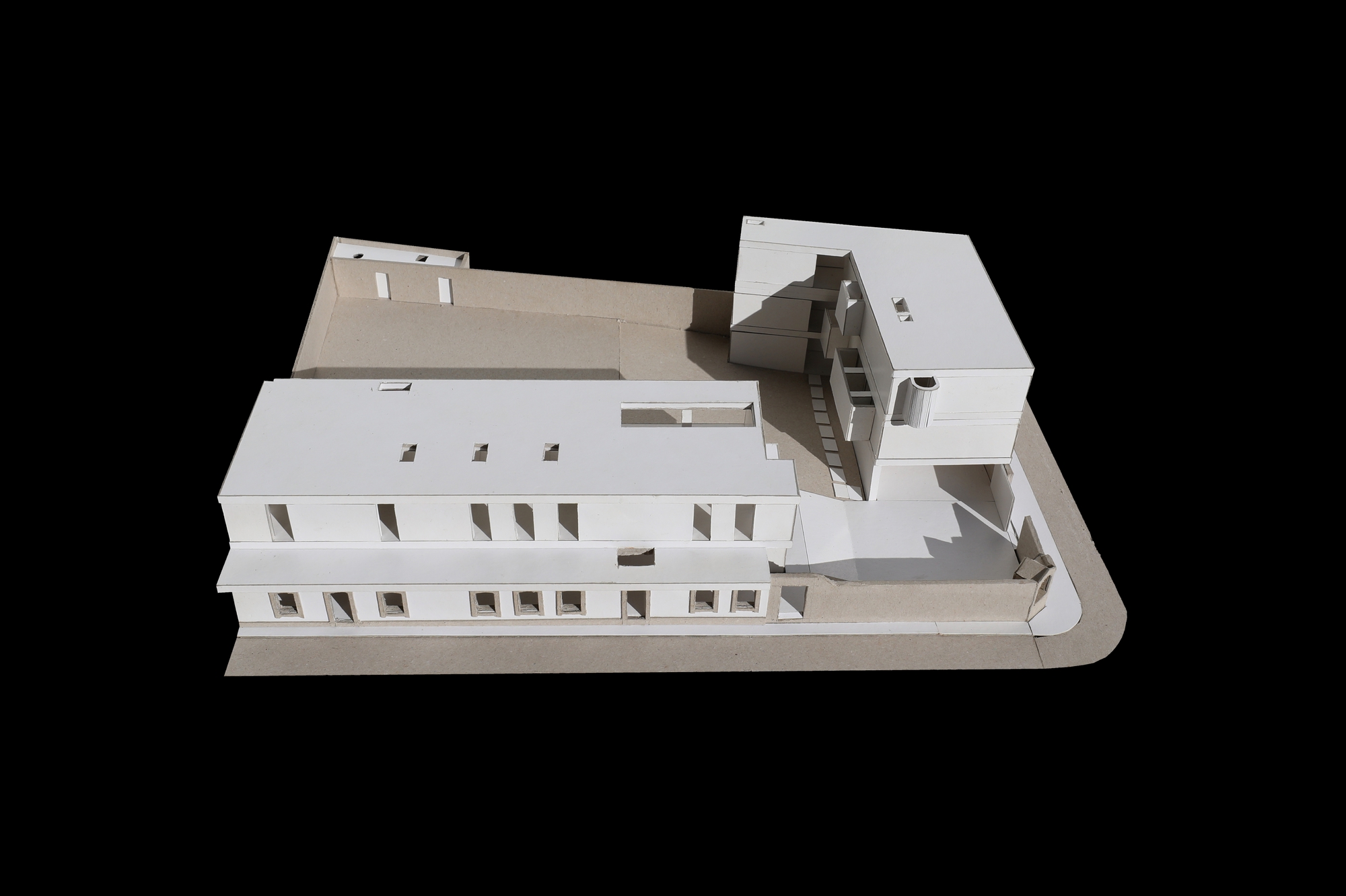 Street side view of the white massing model showing a long two-storey bar with small window openings beside a taller corner block