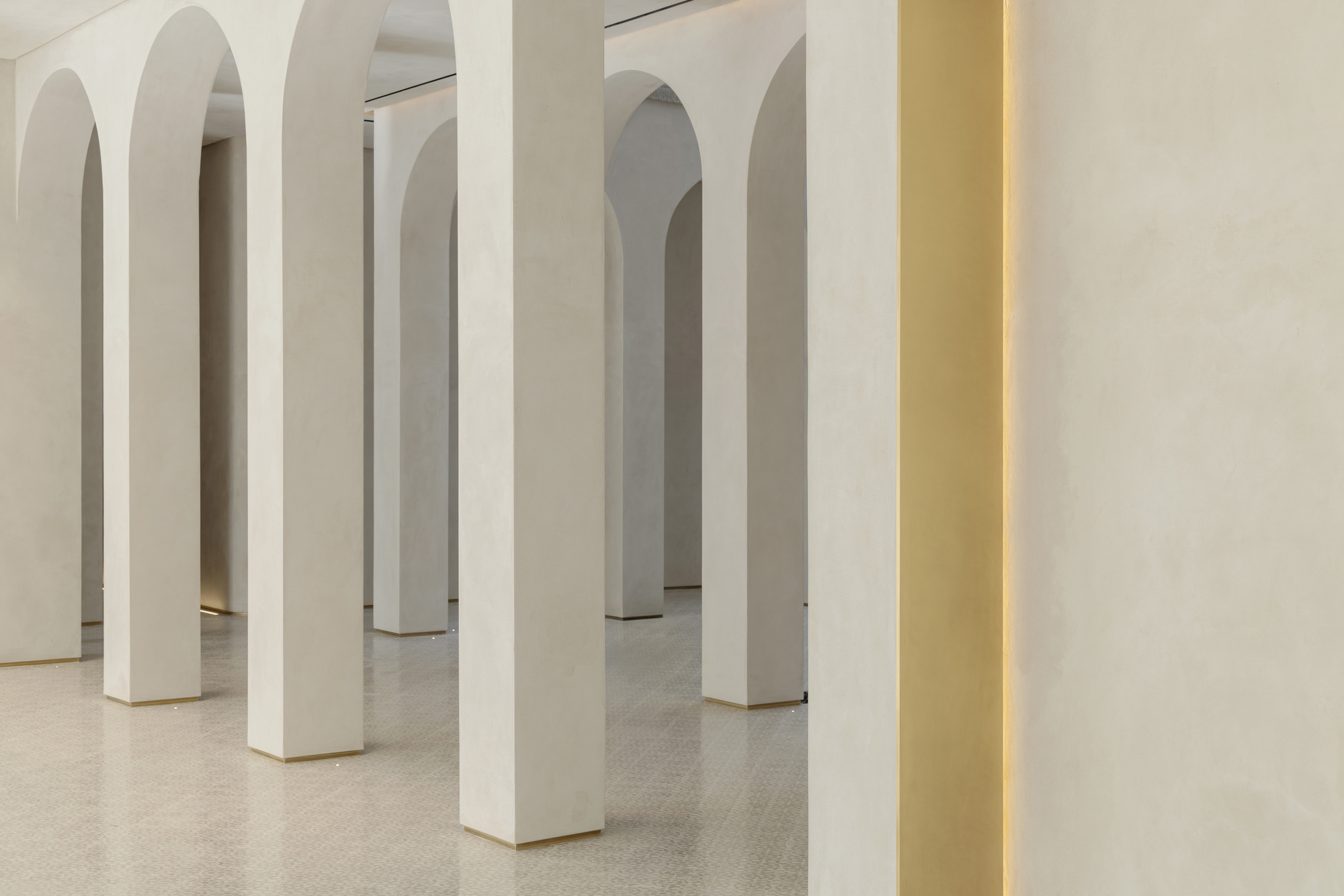 Row of plastered arched columns on a patterned floor, with a brass-lit recess glowing at the right edge