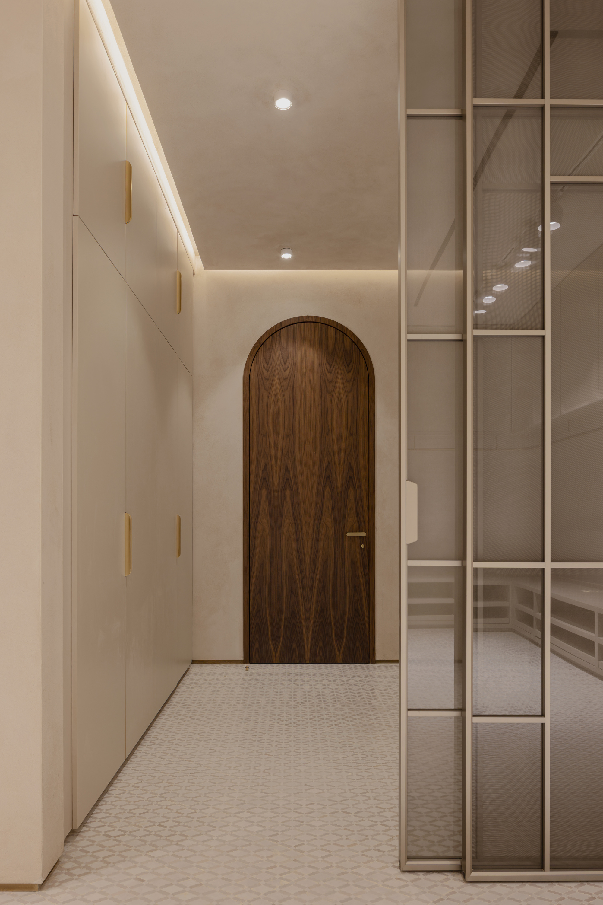Arched walnut door at the end of a corridor, flanked by built-in cabinets and a steel-framed glass partition