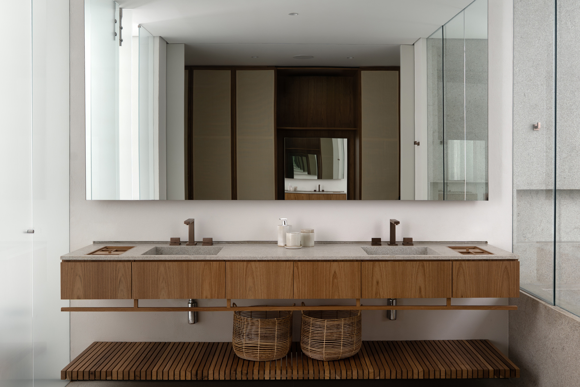 Double vanity with oak drawer fronts, stone countertop and slatted timber shelf holding two woven baskets, reflected in a wide mirror