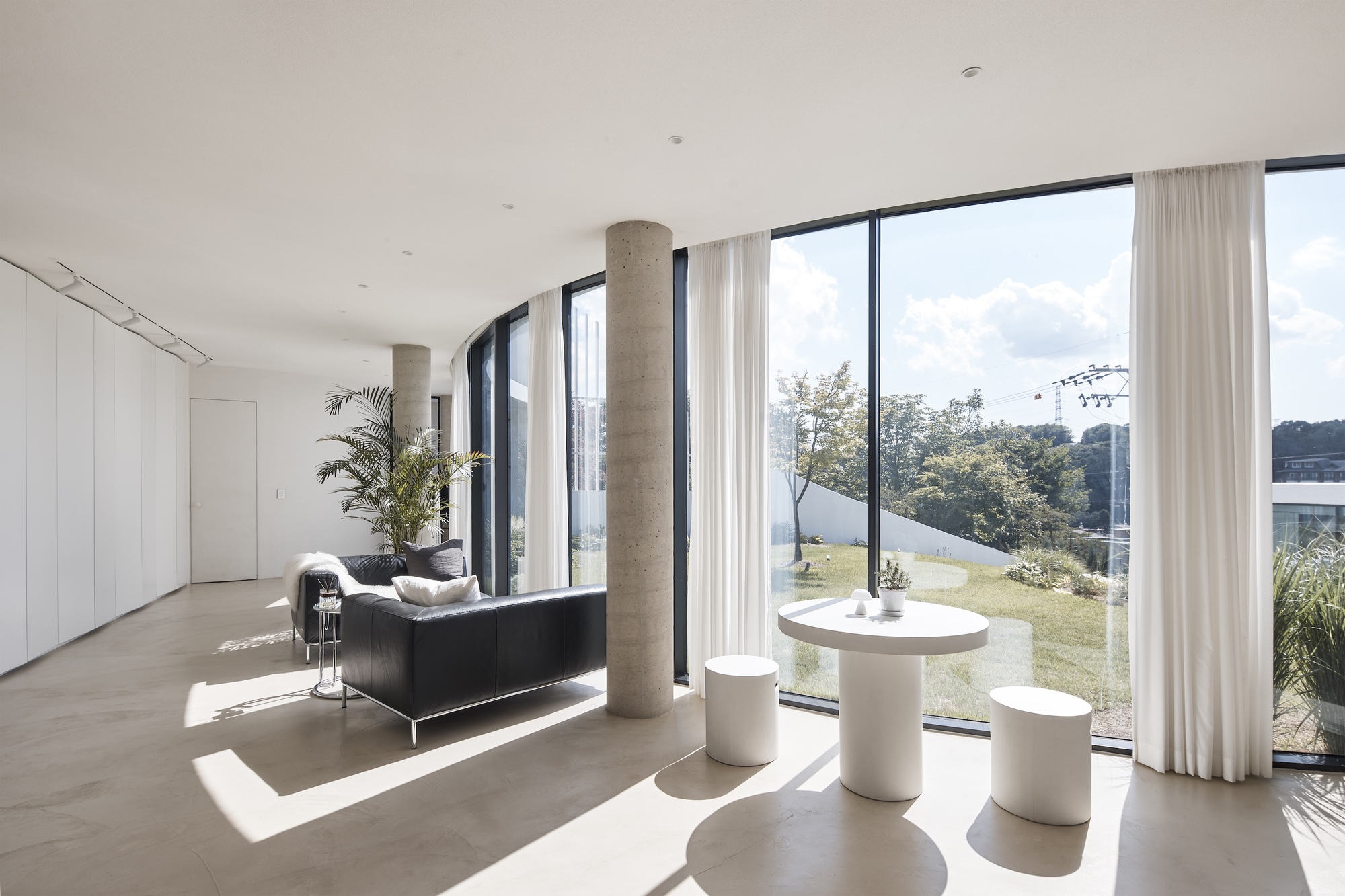 Living area with a round white table and stools, sunlight casting window shadows across the polished concrete floor