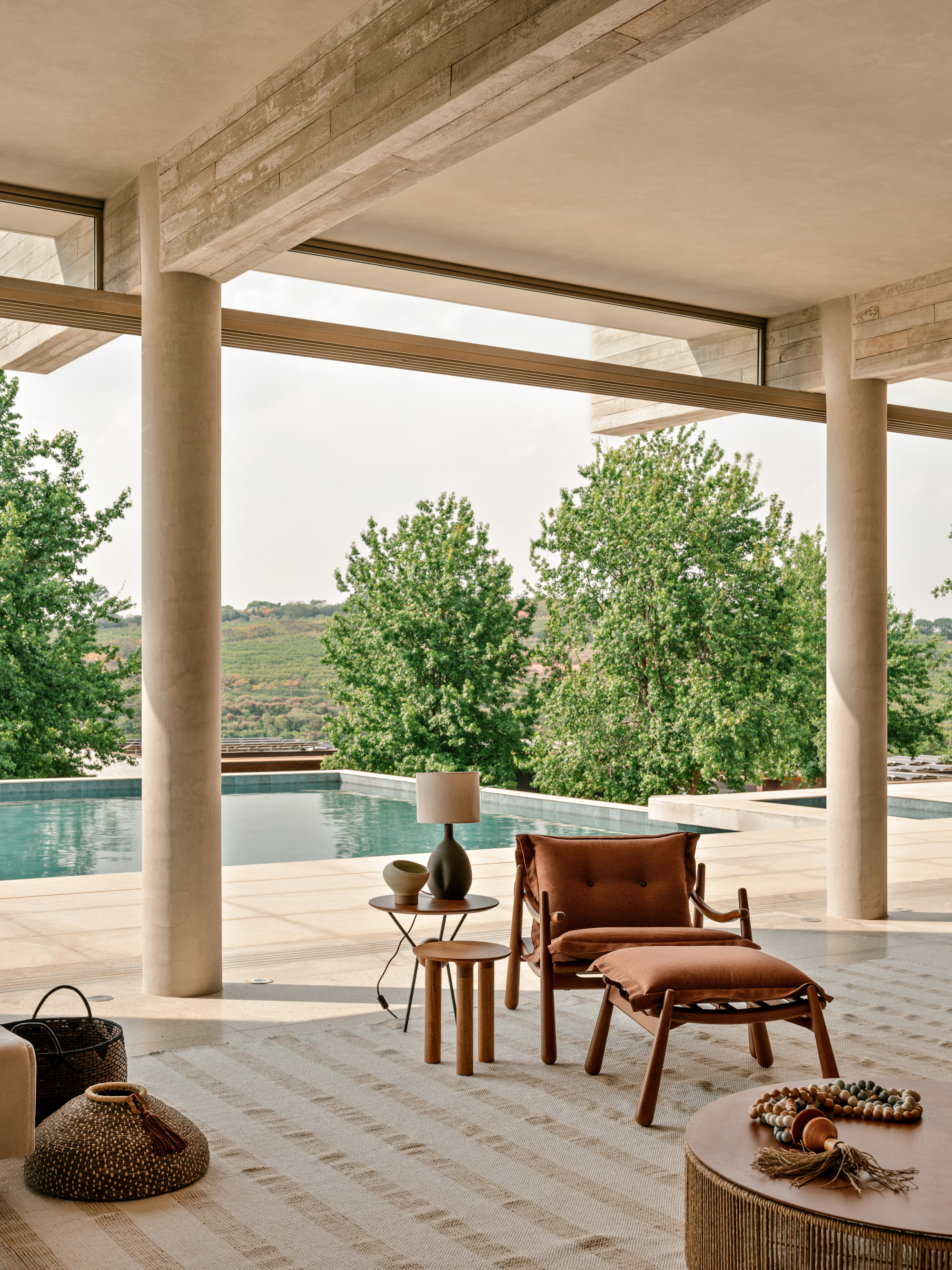 Covered terrace with round concrete columns, a leather lounge chair and side tables facing a pool and green hills