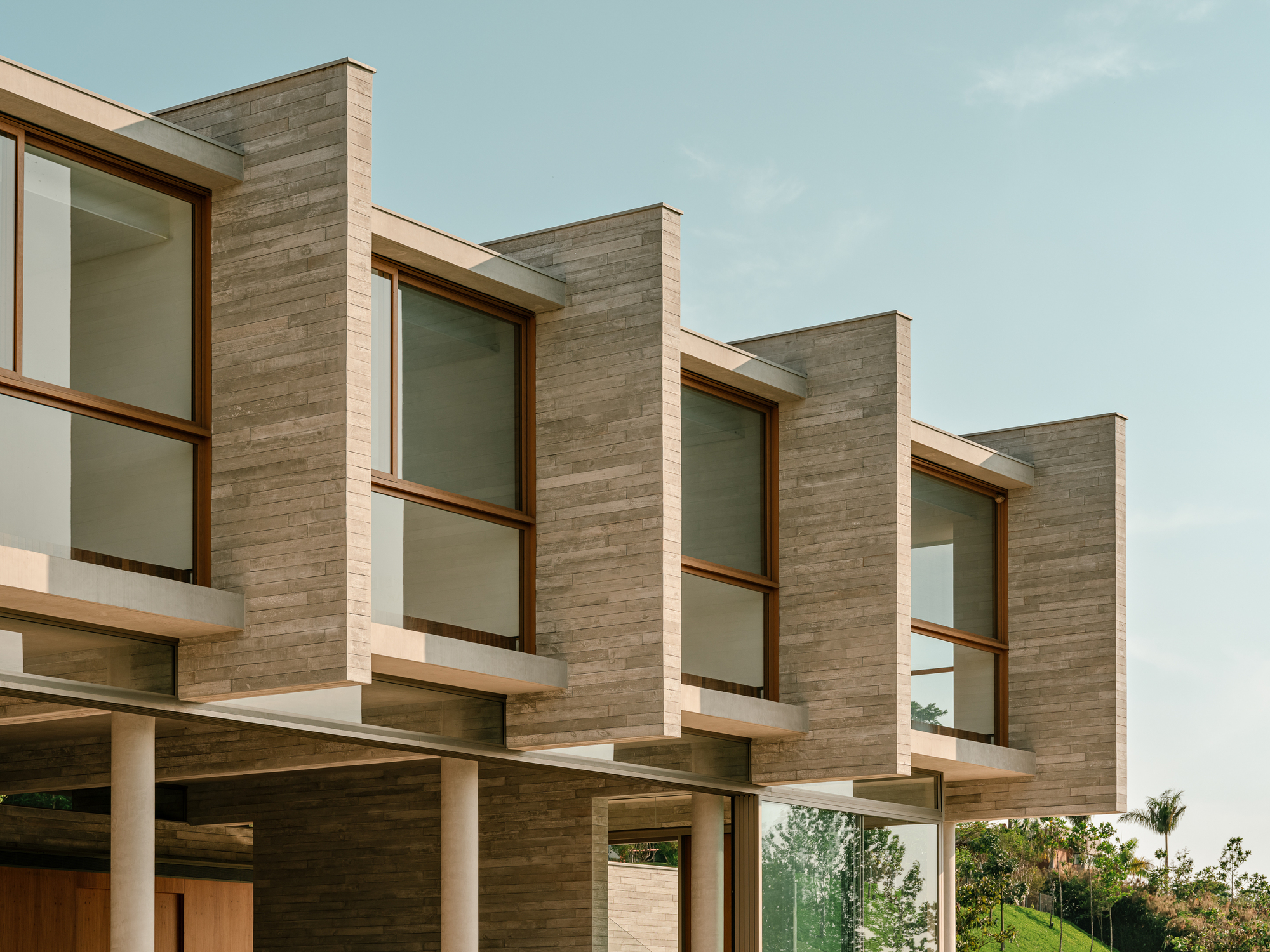 Close-up of staggered concrete fins, timber window frames and slim round columns in warm afternoon light