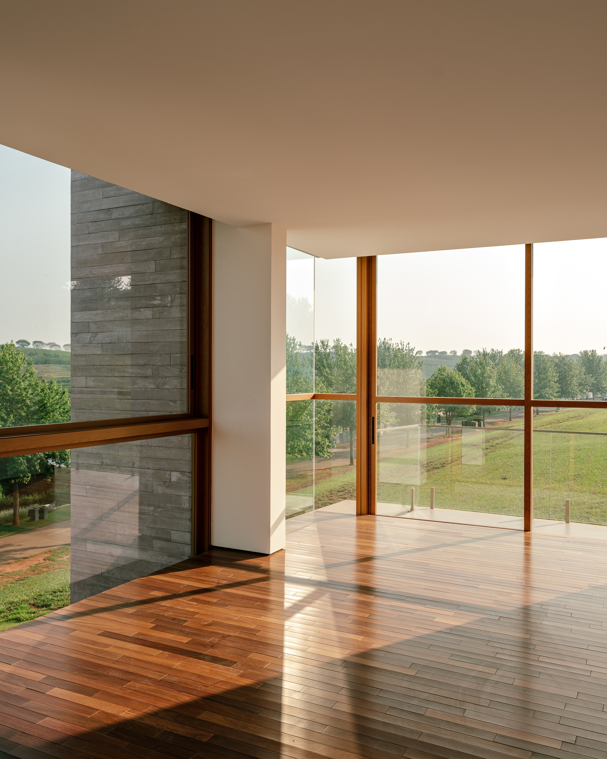 Corner of an upper room with timber-framed glazing, a grey stone wall and a wood plank floor looking onto green lawn