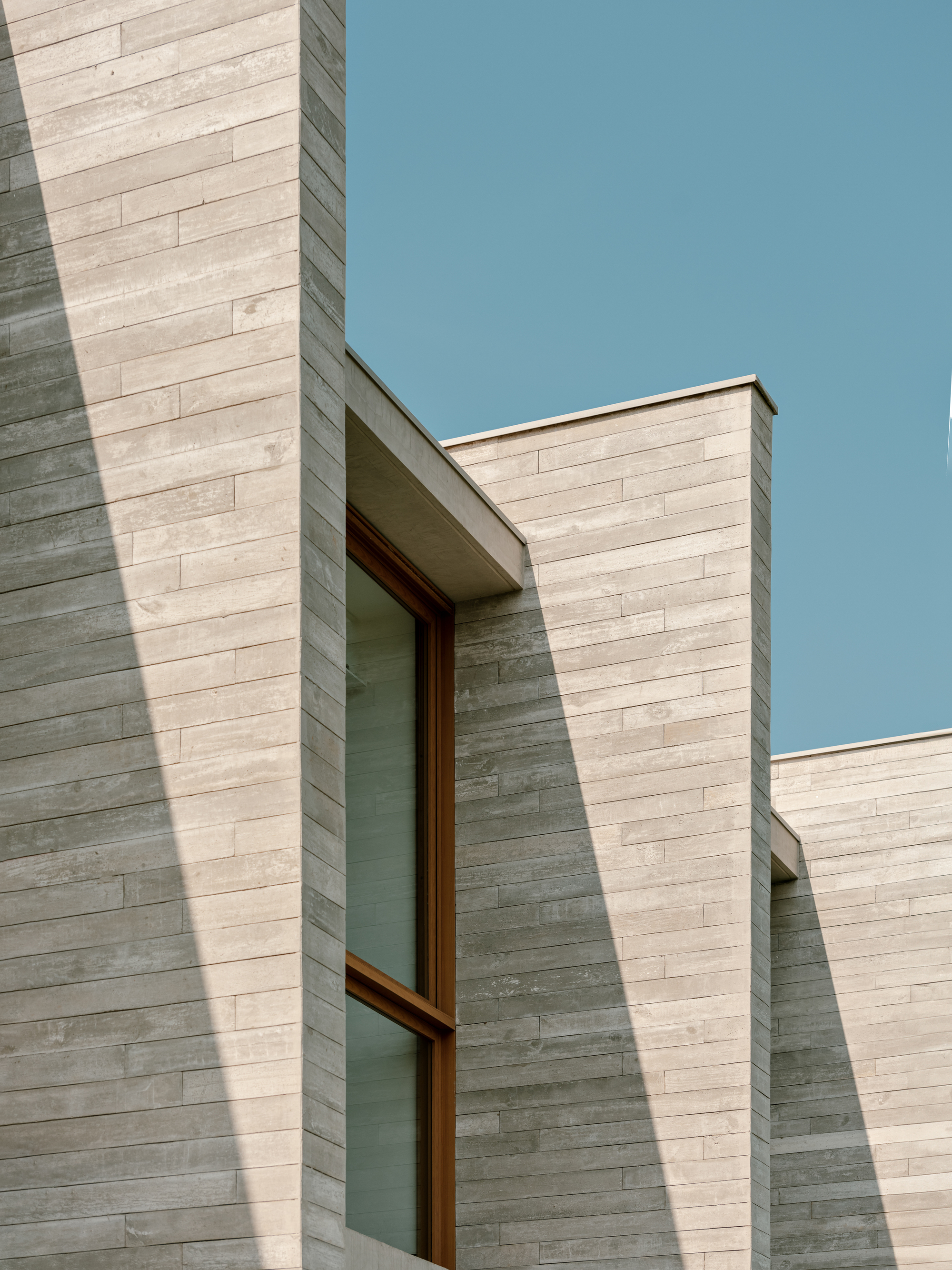 Close-up of horizontal stone cladding with a timber-framed window and a flat roof edge against a clear sky