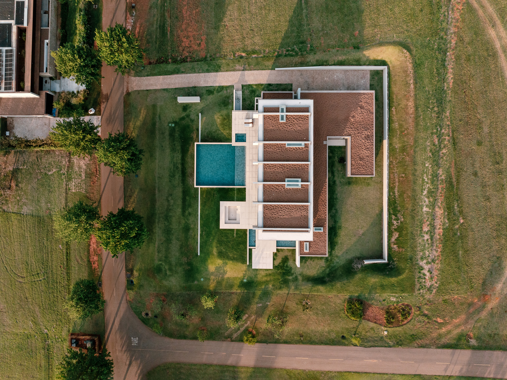 Aerial plan view of a low house with planted roof bands, a rectangular pool and a boundary wall at dusk
