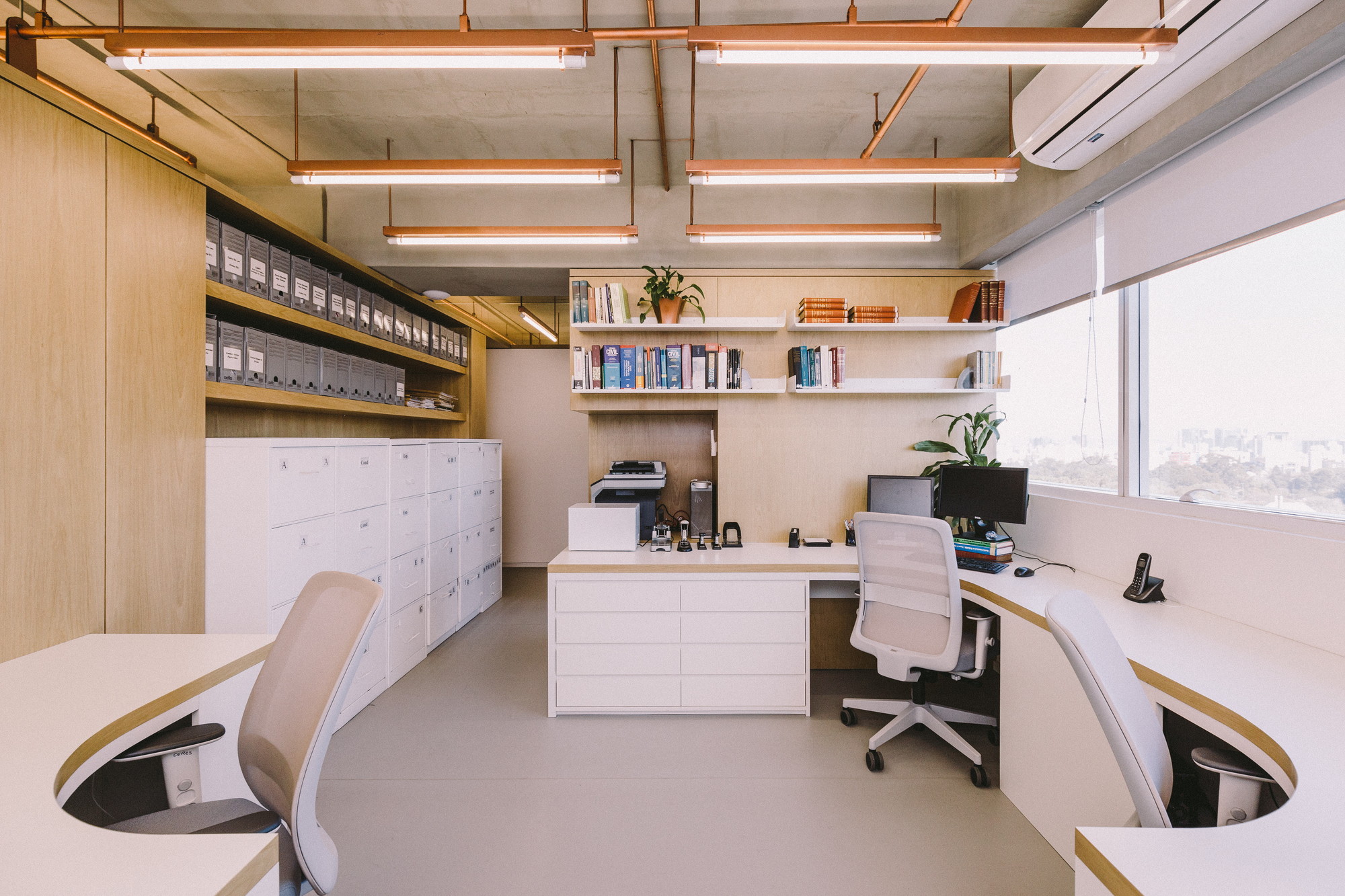 Office workroom with curved white desks, oak shelving of archive boxes and copper-framed light fixtures, daylight entering through the window