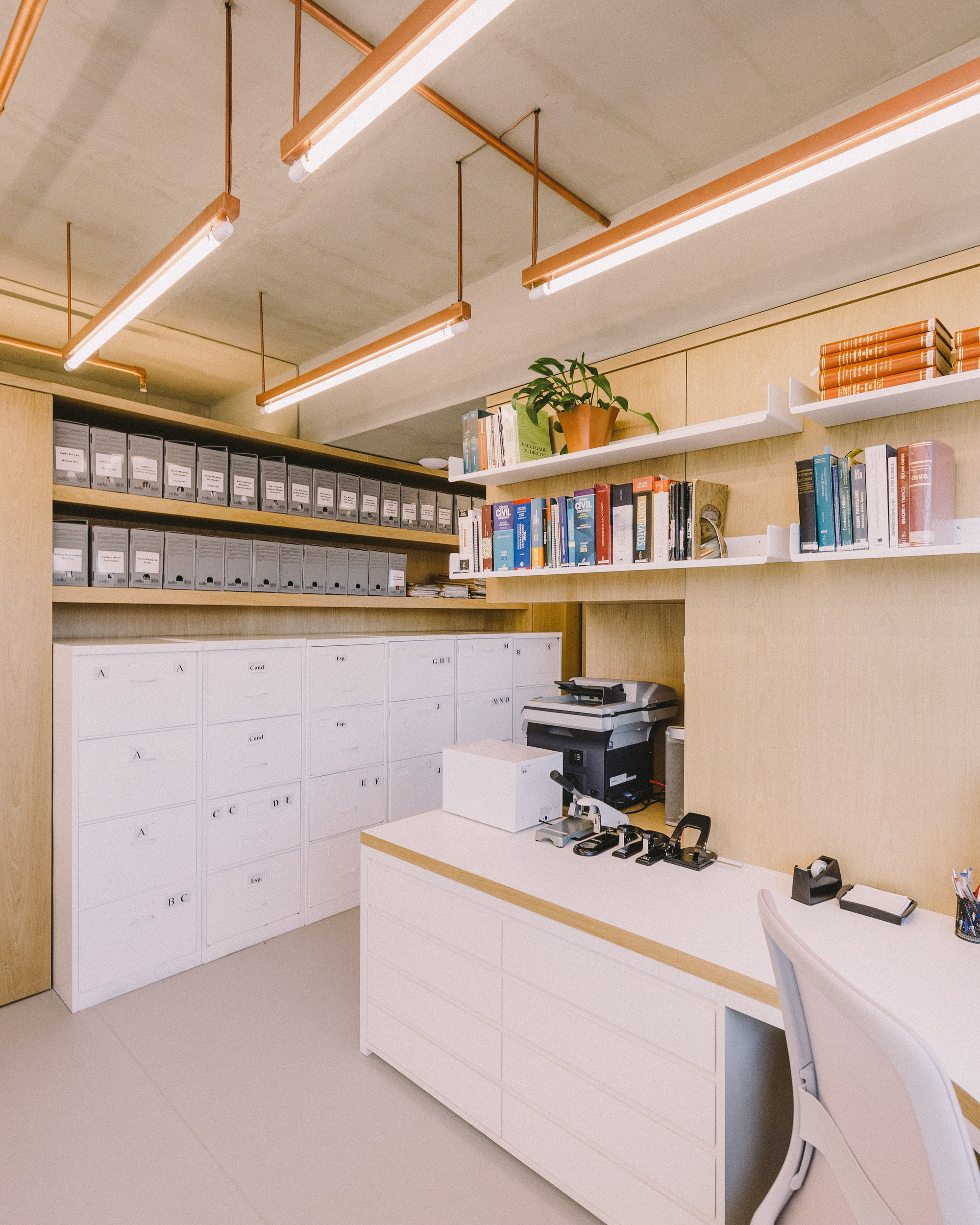 Office corner with white drawer cabinets, archive boxes, a printer and a potted plant under copper pendant lights