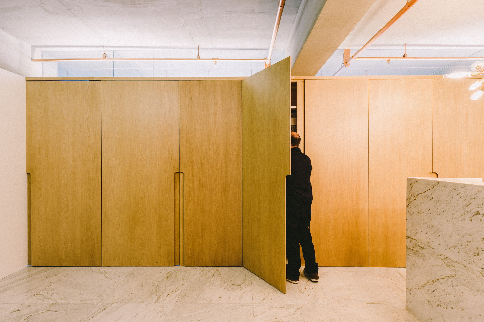 Oak cabinet wall with one tall door swung open and a man reaching inside, beside a marble counter edge
