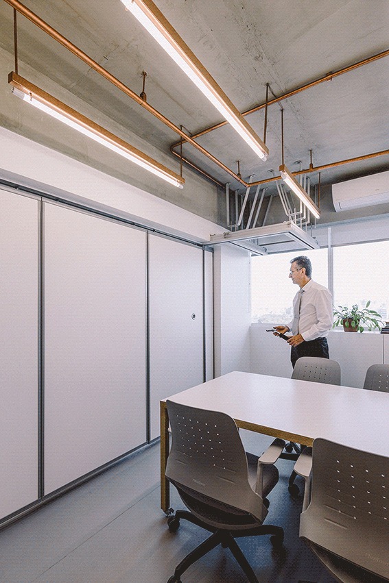 Man in a white shirt standing by the window past a closed white sliding partition, copper pipes running overhead