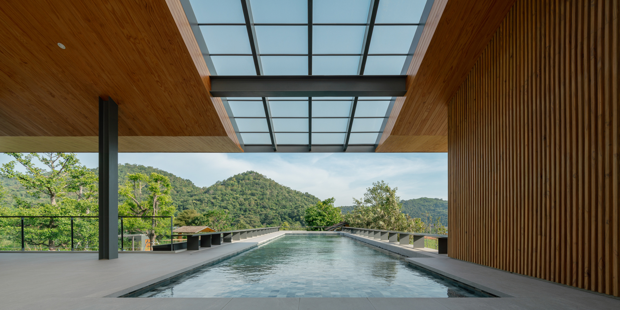 Lap pool beneath a glazed roof slot and timber soffit, framing forested hills in clear daylight