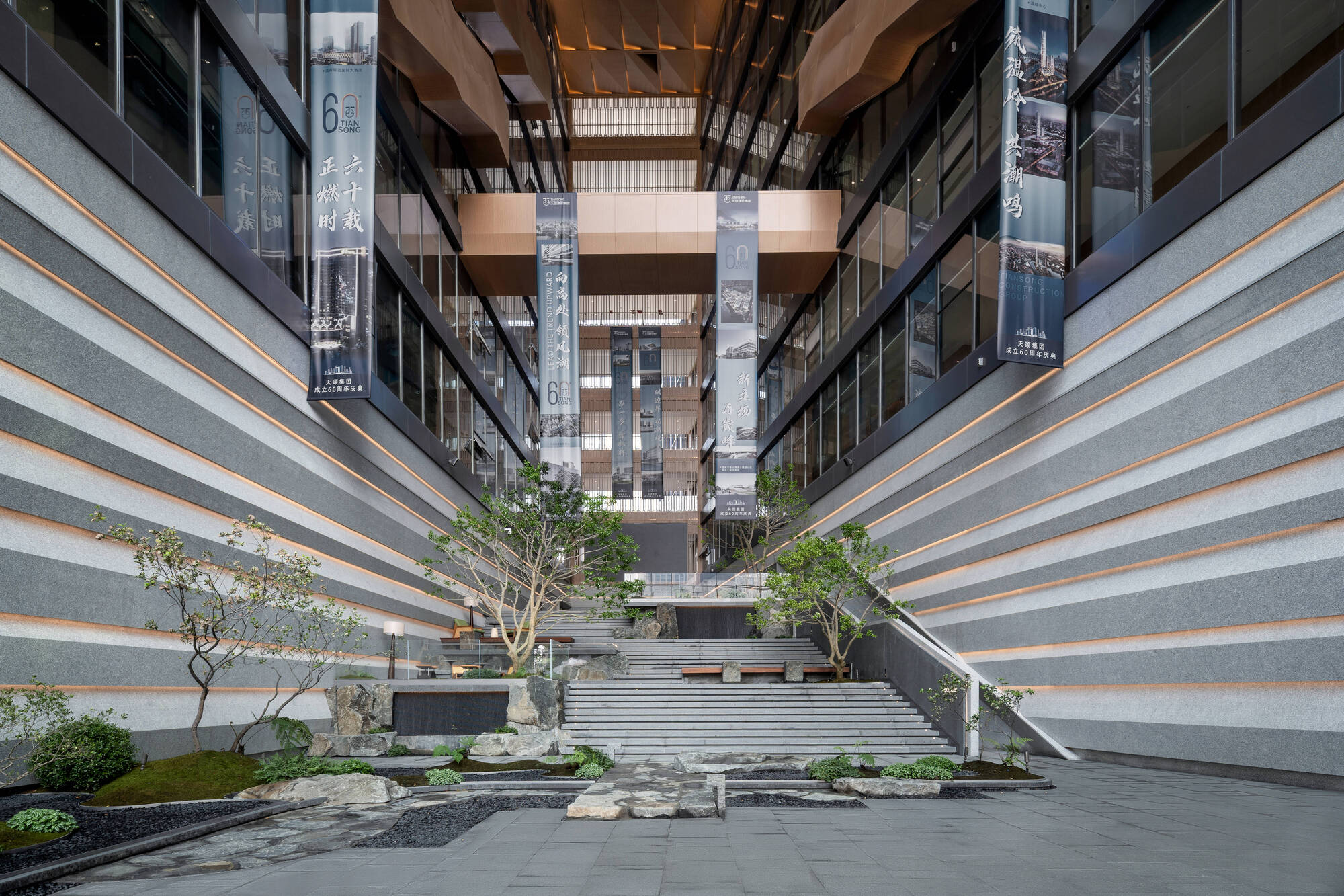 Atrium courtyard with banded stone walls, a stepped stair, rock garden and pine trees beneath bronze-clad overhangs