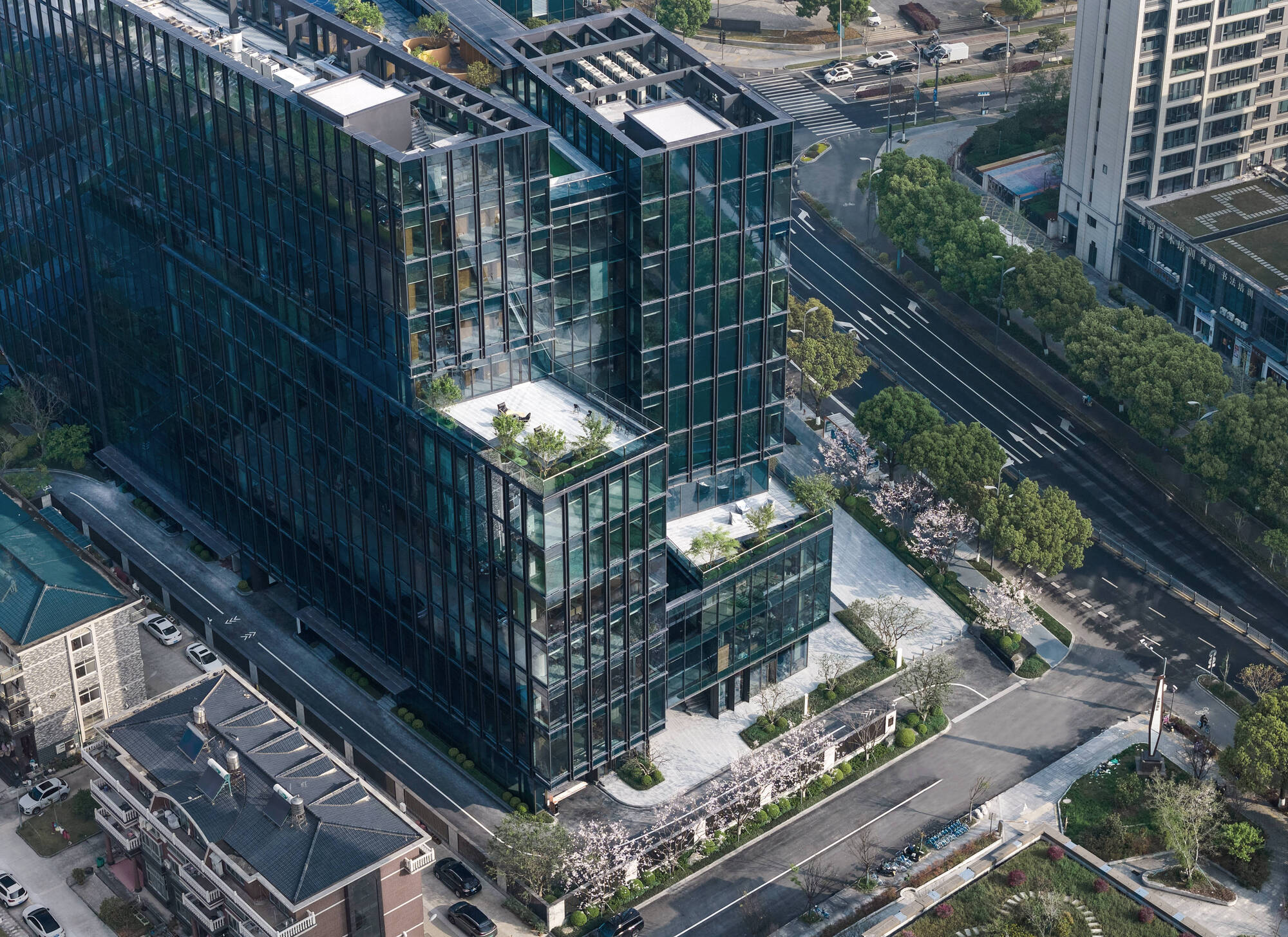 Aerial view of the terraced glass volumes with planted rooftop gardens and blossoming trees along the surrounding streets
