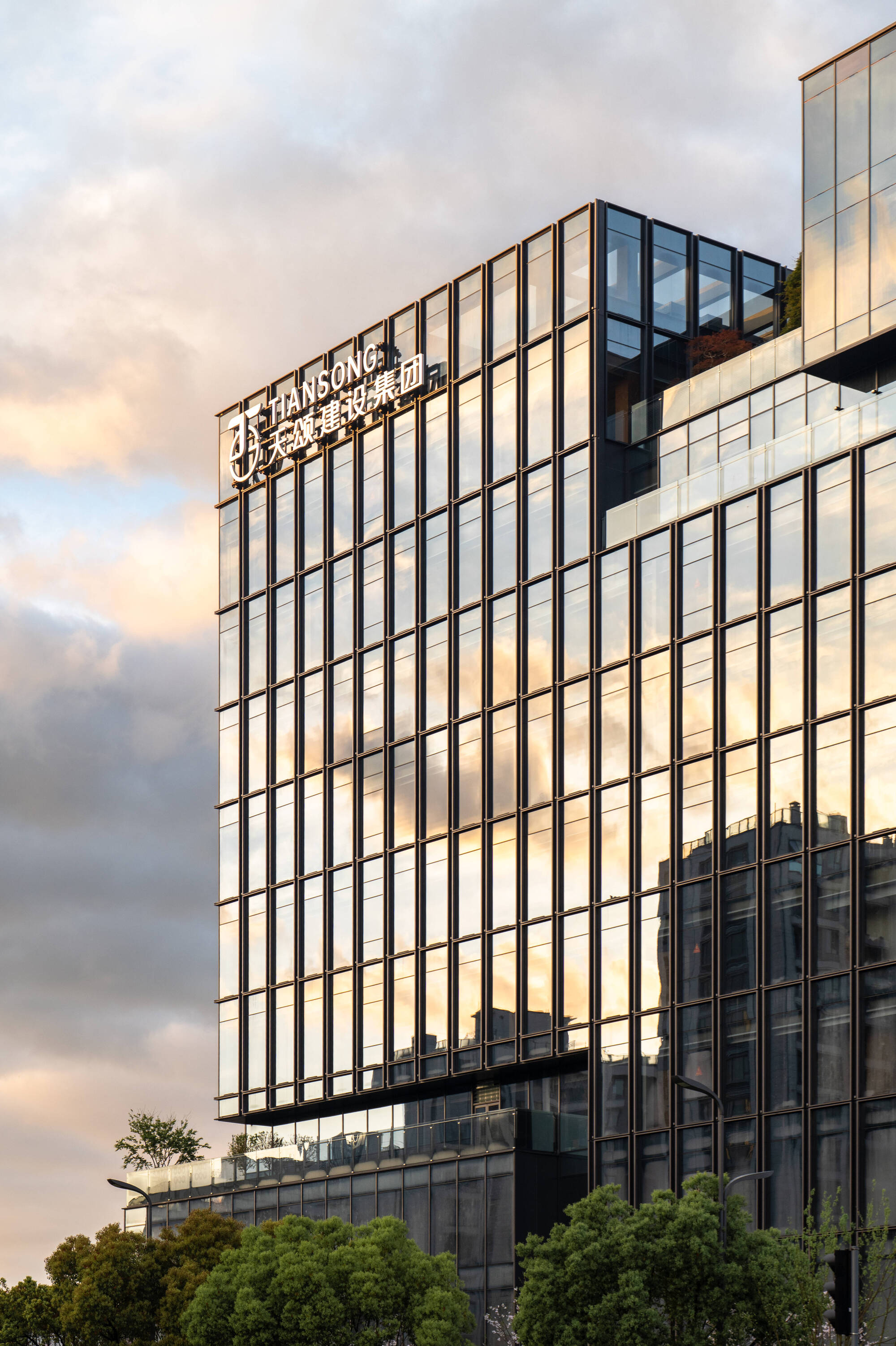 Upper floors of the glass tower with rooftop signage, reflecting pink clouds and neighbouring buildings in warm sunset light