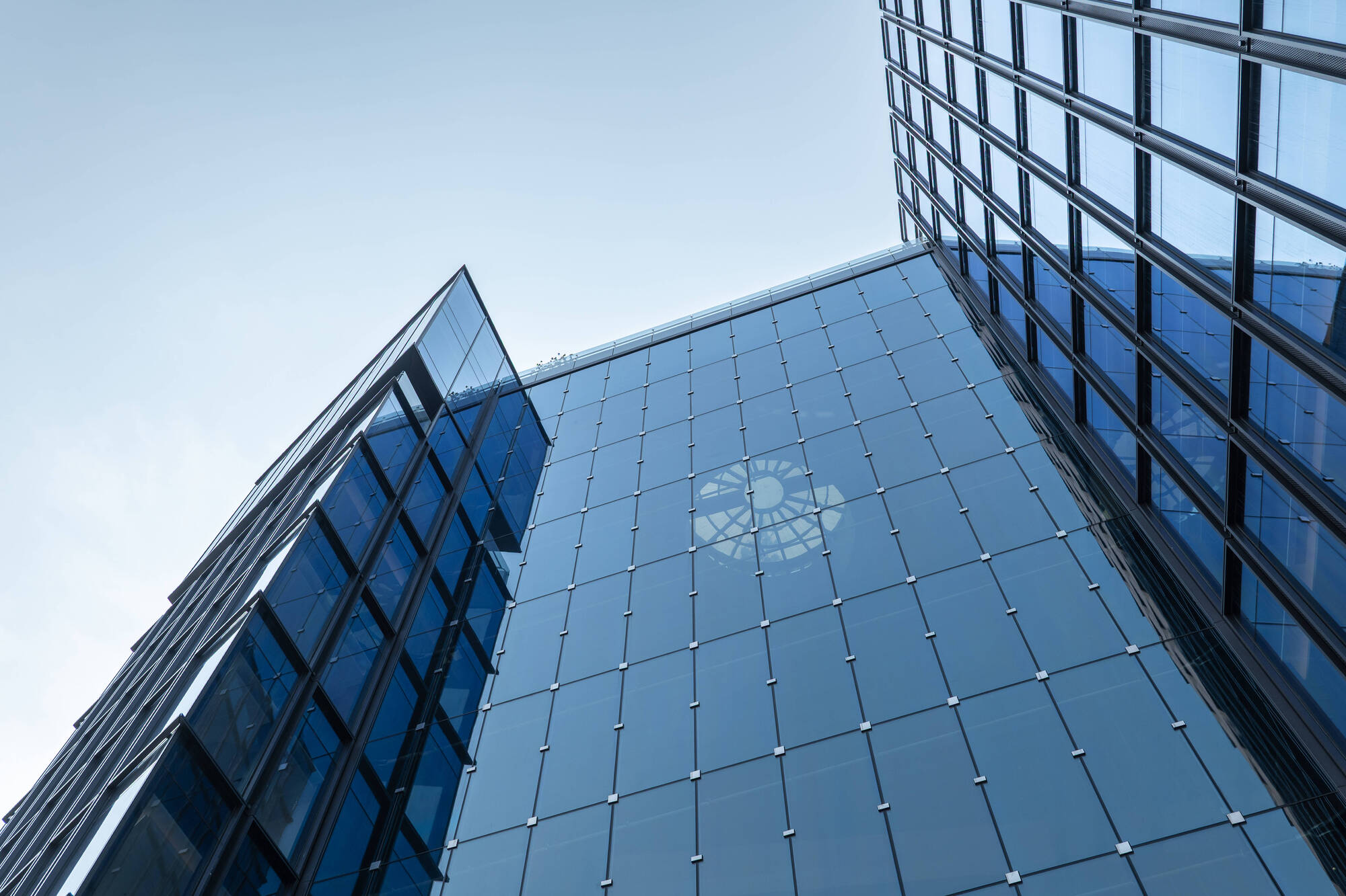 Looking up at two glass tower corners meeting at an angle, with a circular reflection on the blue facade