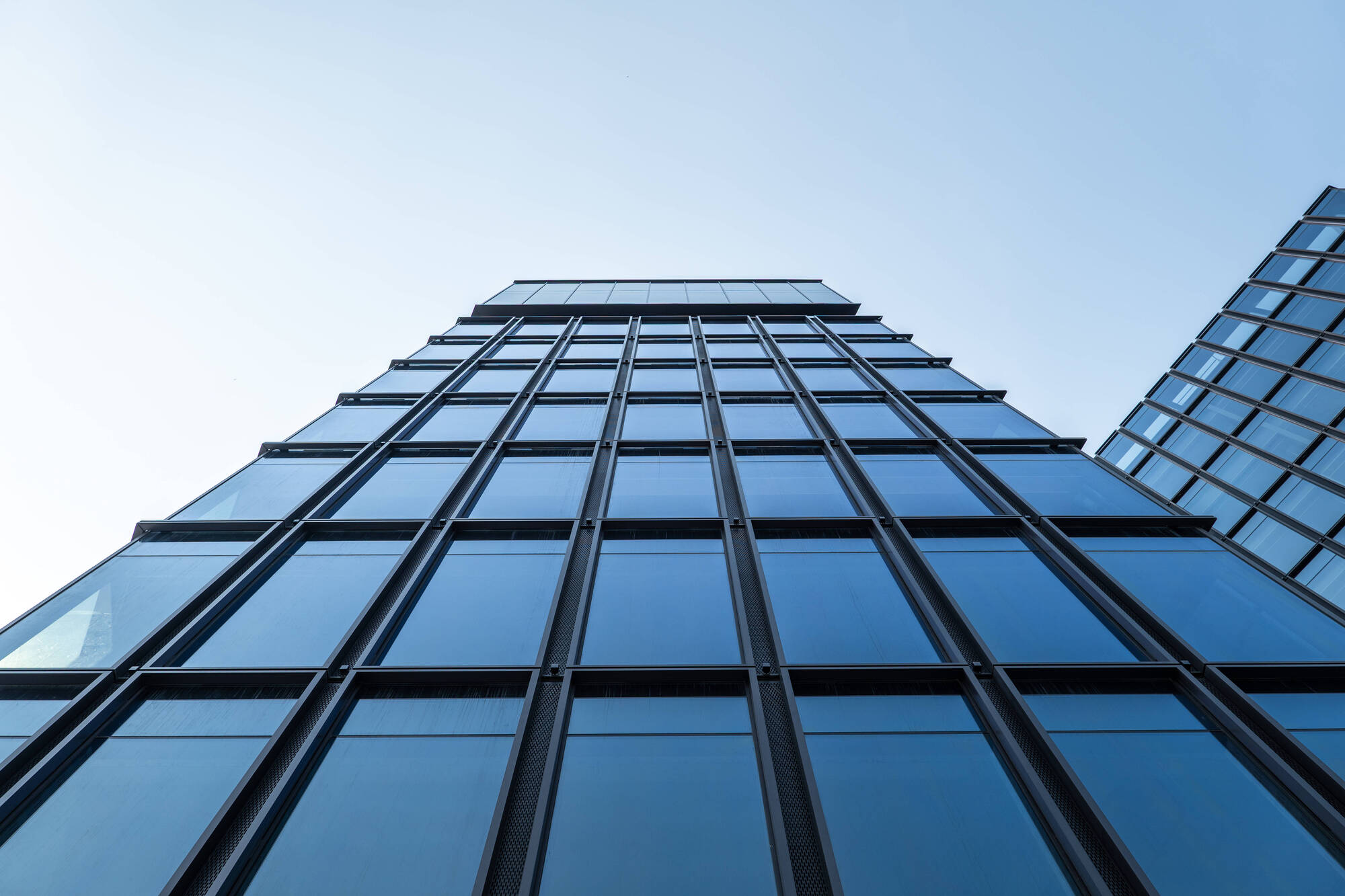 Worm's-eye view of the stepped glass facade with dark vertical fins rising toward a clear pale sky