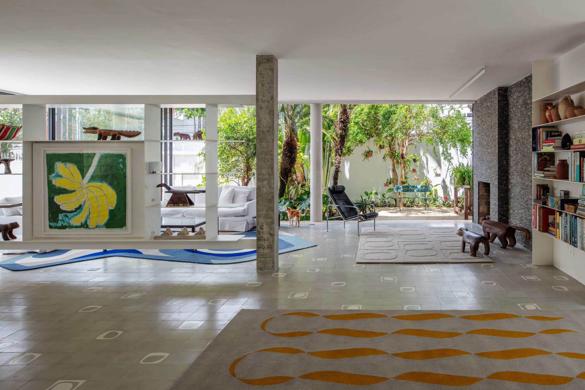 Open living area with a concrete column, patterned rugs and a stone fireplace facing a planted garden in daylight