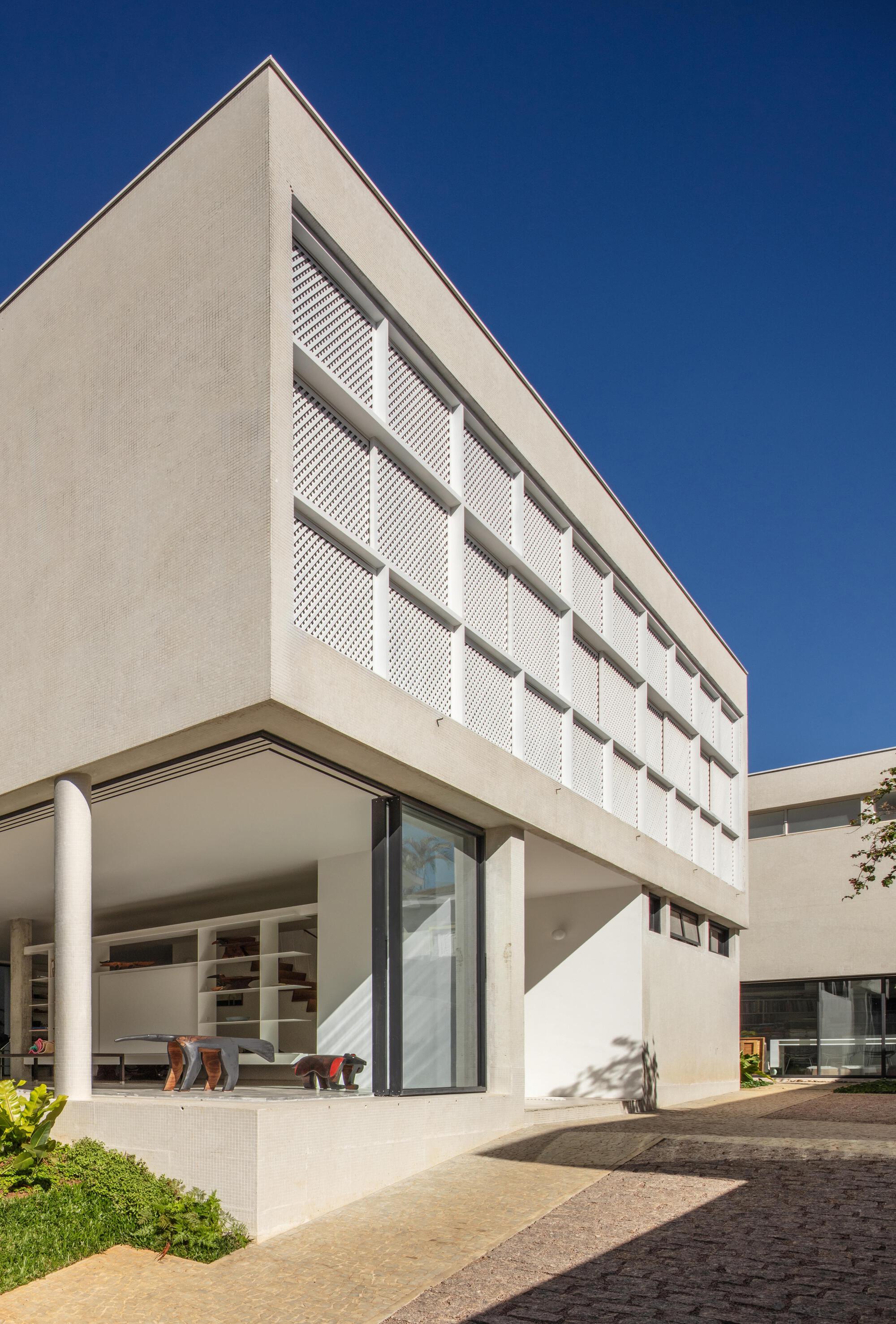 Corner of the white upper volume with lattice screen panels above a glazed ground floor under a deep blue sky
