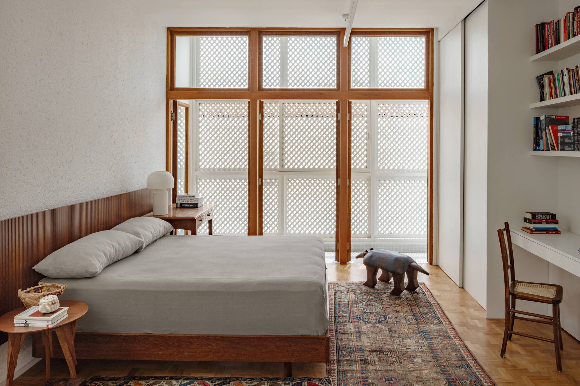 Bedroom with timber-framed lattice screen doors, a wood-headed bed and a patterned rug in soft daylight