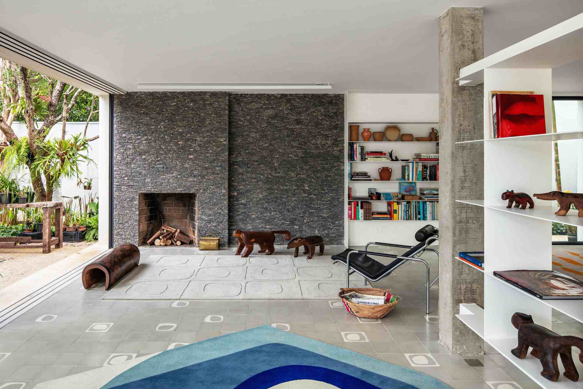 Living area with a dark stone fireplace wall, a black leather lounge chair and carved wooden animals, opening to a garden