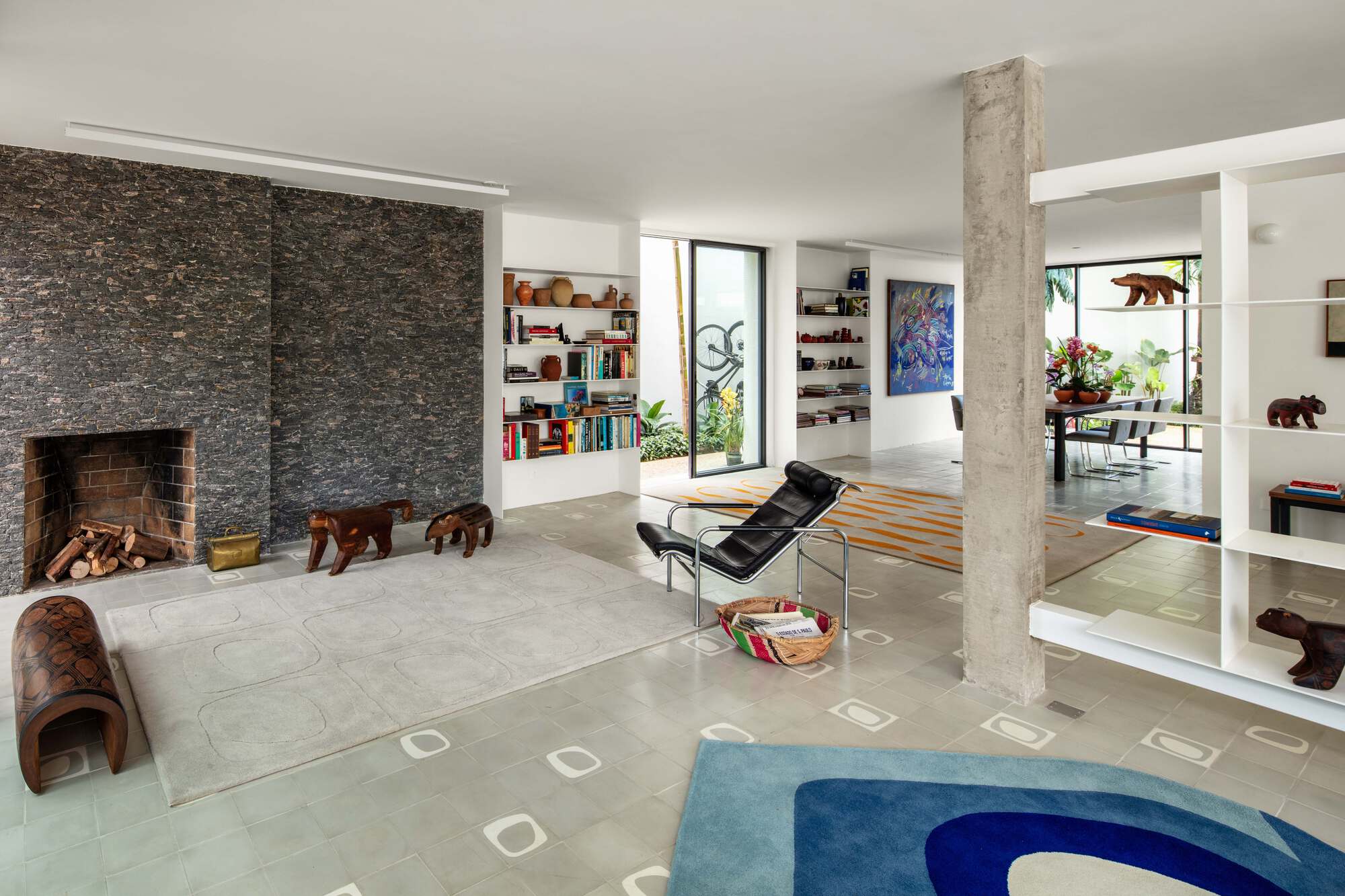 Wide view of the living room with fireplace, concrete column, blue rug and patterned floor tiles leading to the dining area