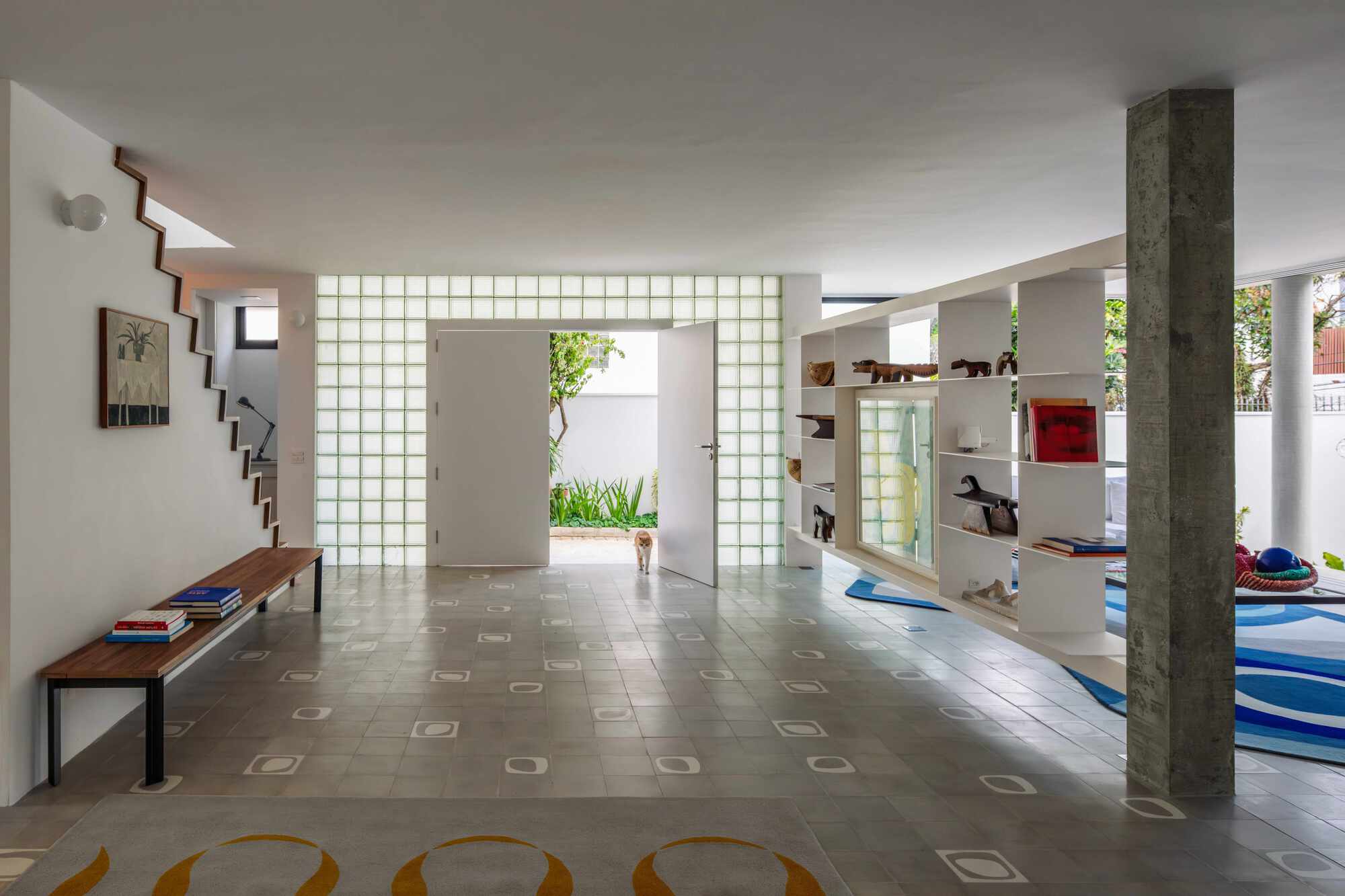 Ground floor entry hall with glass block wall, open white door, zigzag stair and shelving divider, a small dog standing in the garden light