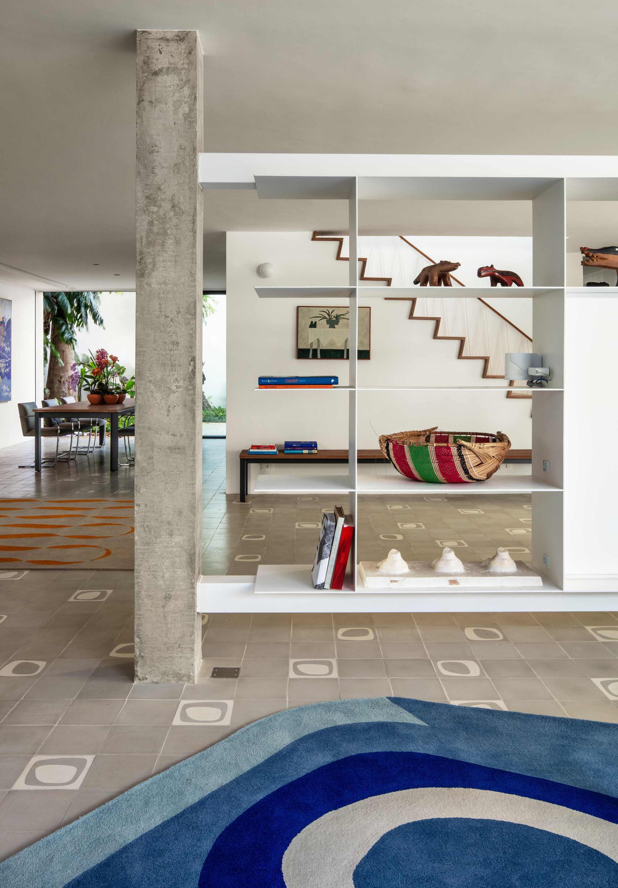 Board-formed concrete column beside a white shelving divider holding a striped basket and wooden animals, with a blue rug in the foreground